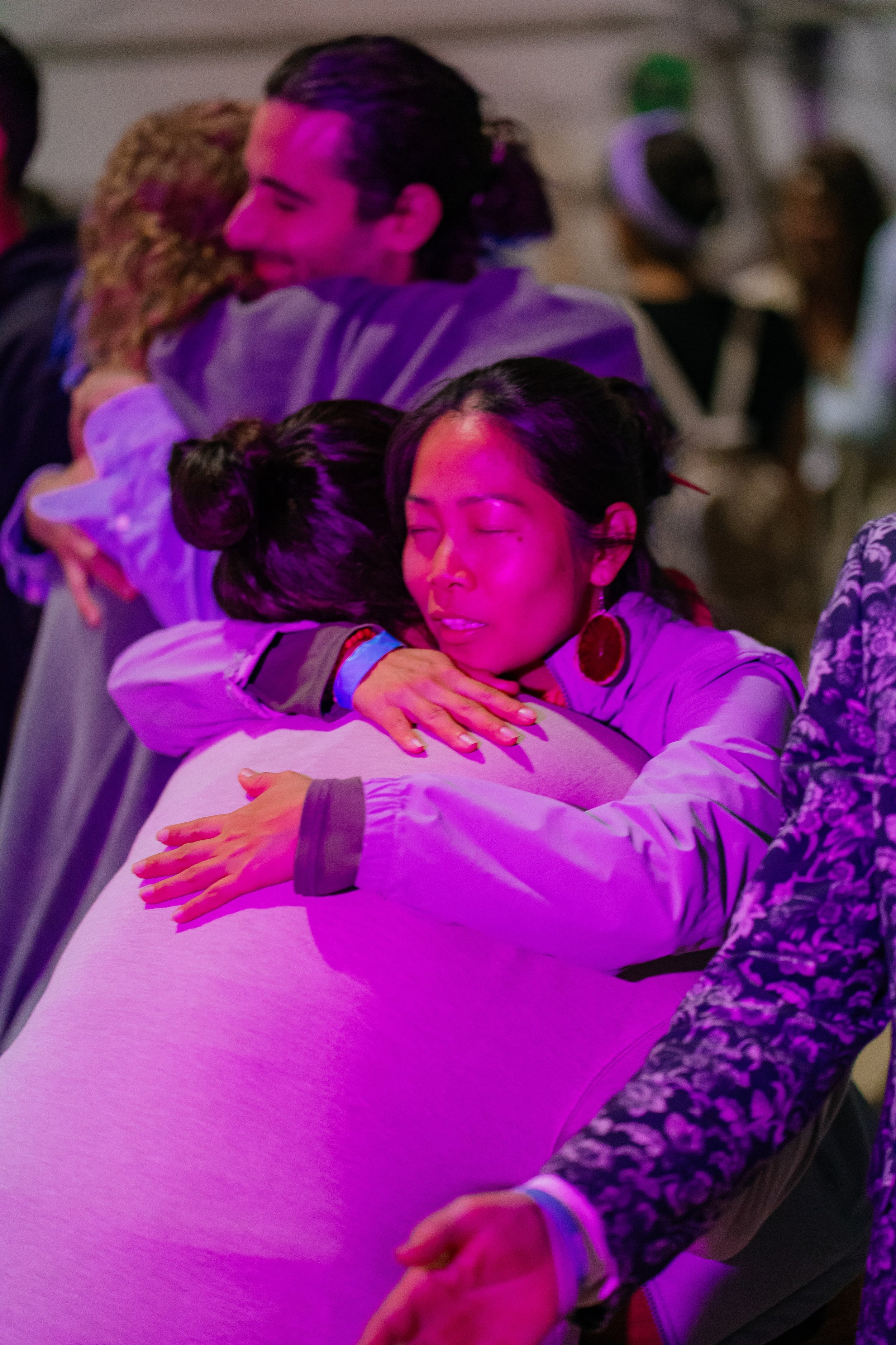 People hugging at a gathering with pink and purple lighting.