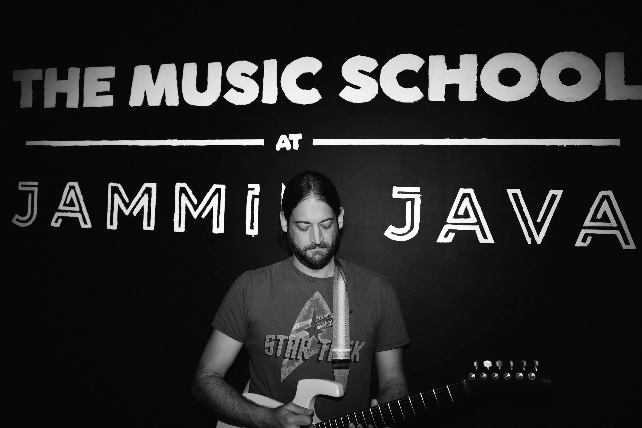 Brad Macpherson pictured in front of a music school sign with an electric guitar
