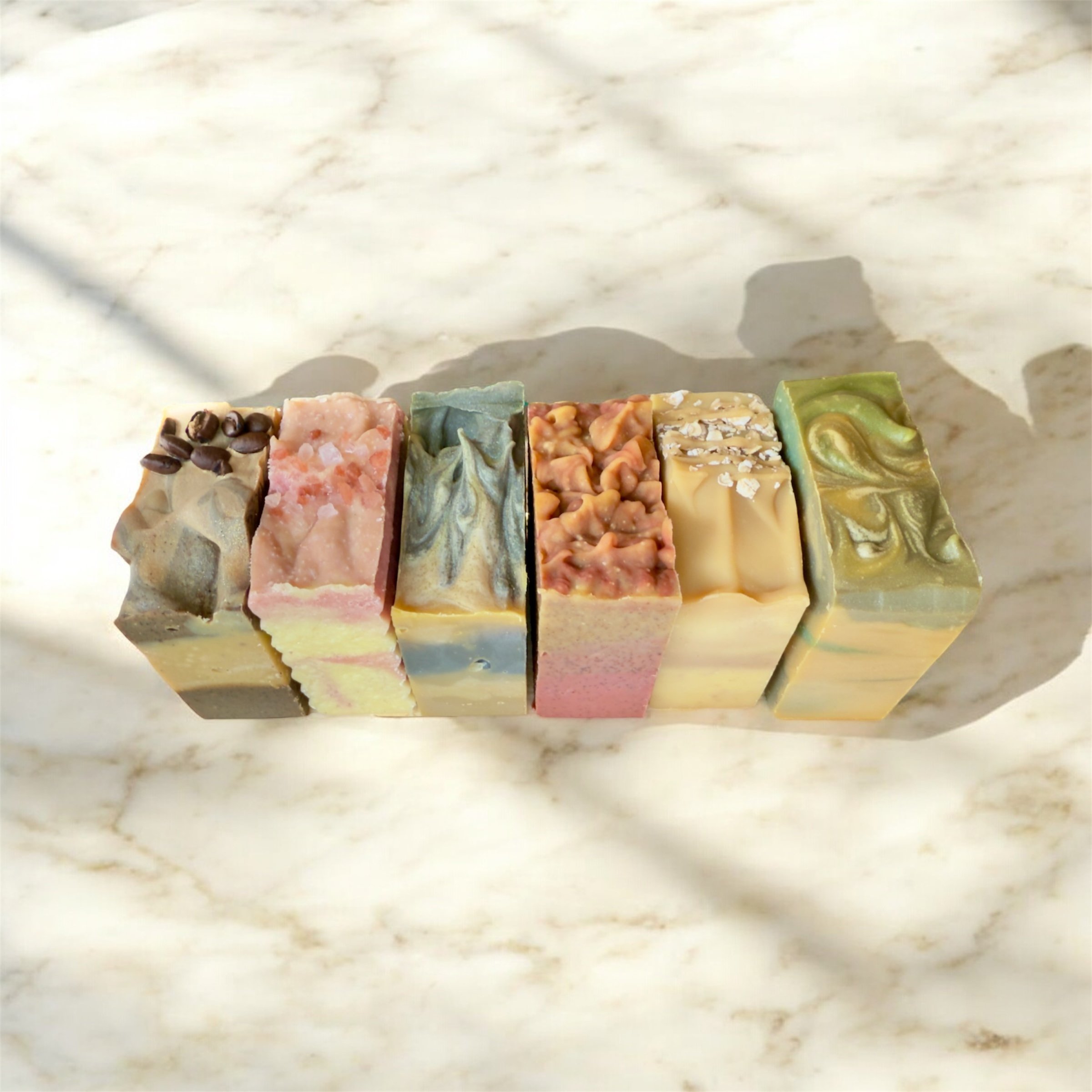 Six colorful handmade soap bars arranged in a row on a light marble surface.