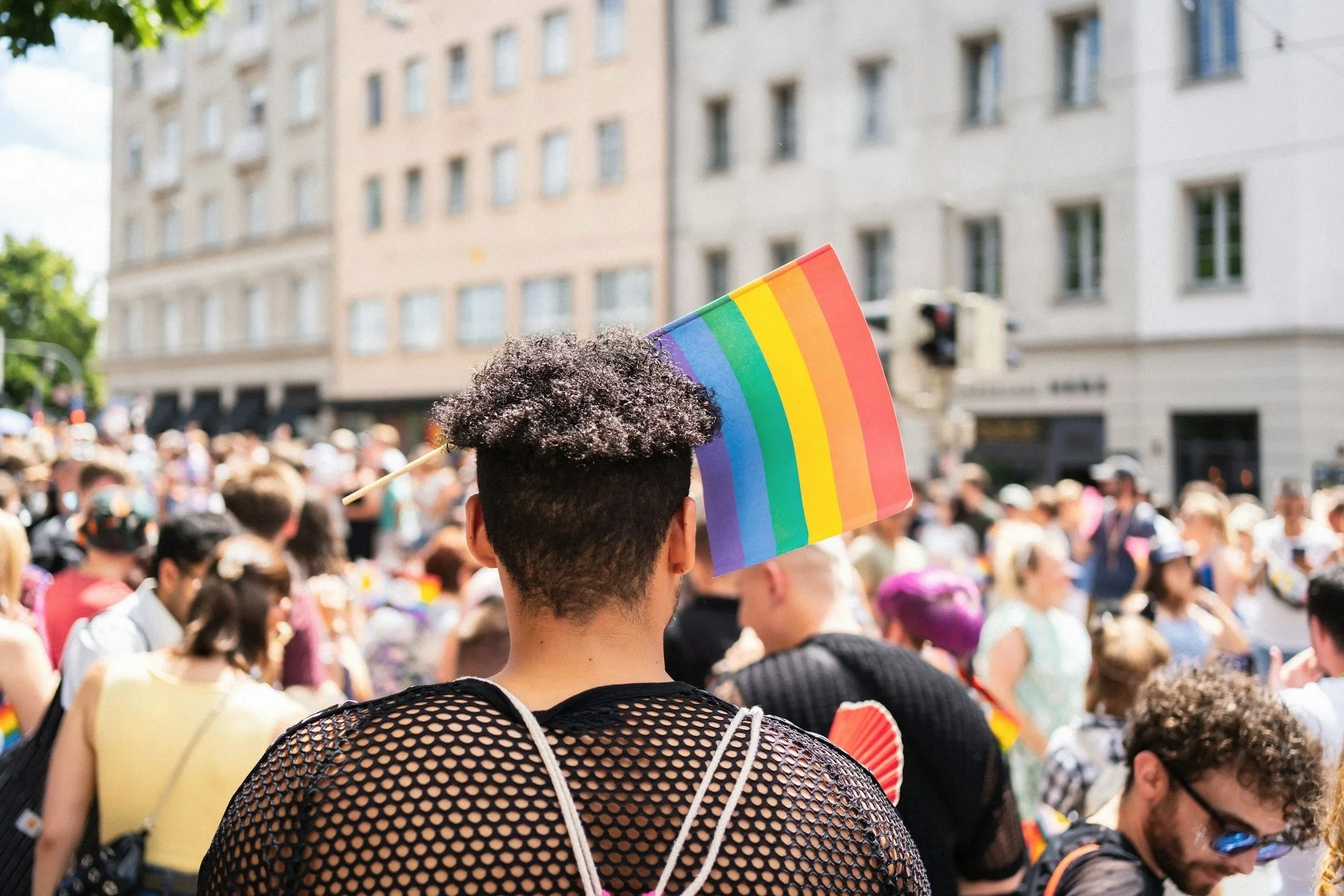 Person viewed from behind holding an LGBTQIA+ pride flag at a pride event, representing LGBTQIA+ affirming therapy and a supportive space for identity exploration.