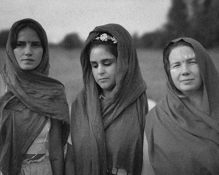 Three women in headscarves standing outdoors in a field, with serious expressions.