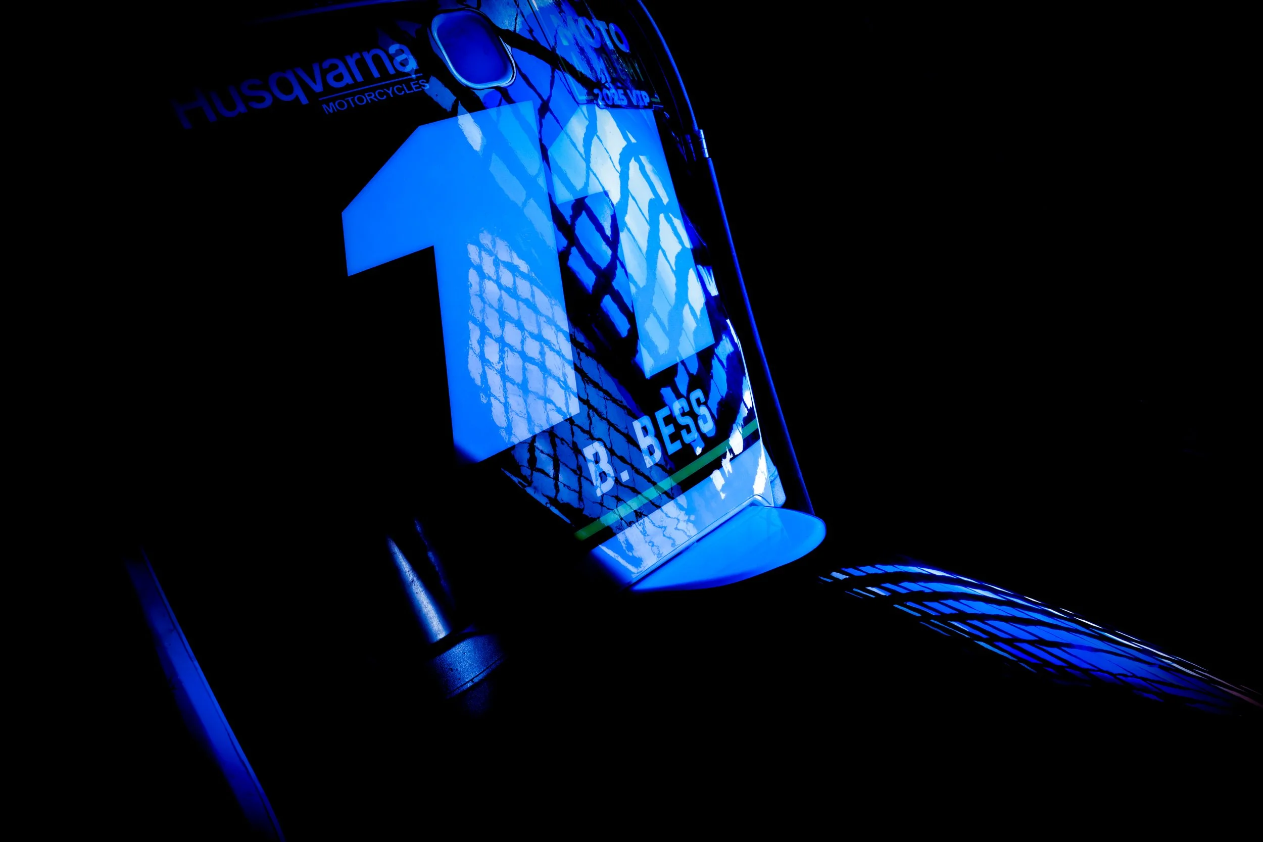 Close-up of a digital display showing the number 12 in blue, with the text 'Husqvarna Motorcycles' and 'B. BESS' visible, against a dark background.