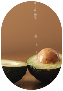 Two halved avocados, one with a seed, with a stream of liquid pouring onto them.