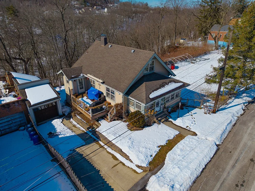 A large white mansion with multiple roof sections and balconies, surrounded by green lawn and trees, with a swimming pool and outdoor lounge area in the backyard.