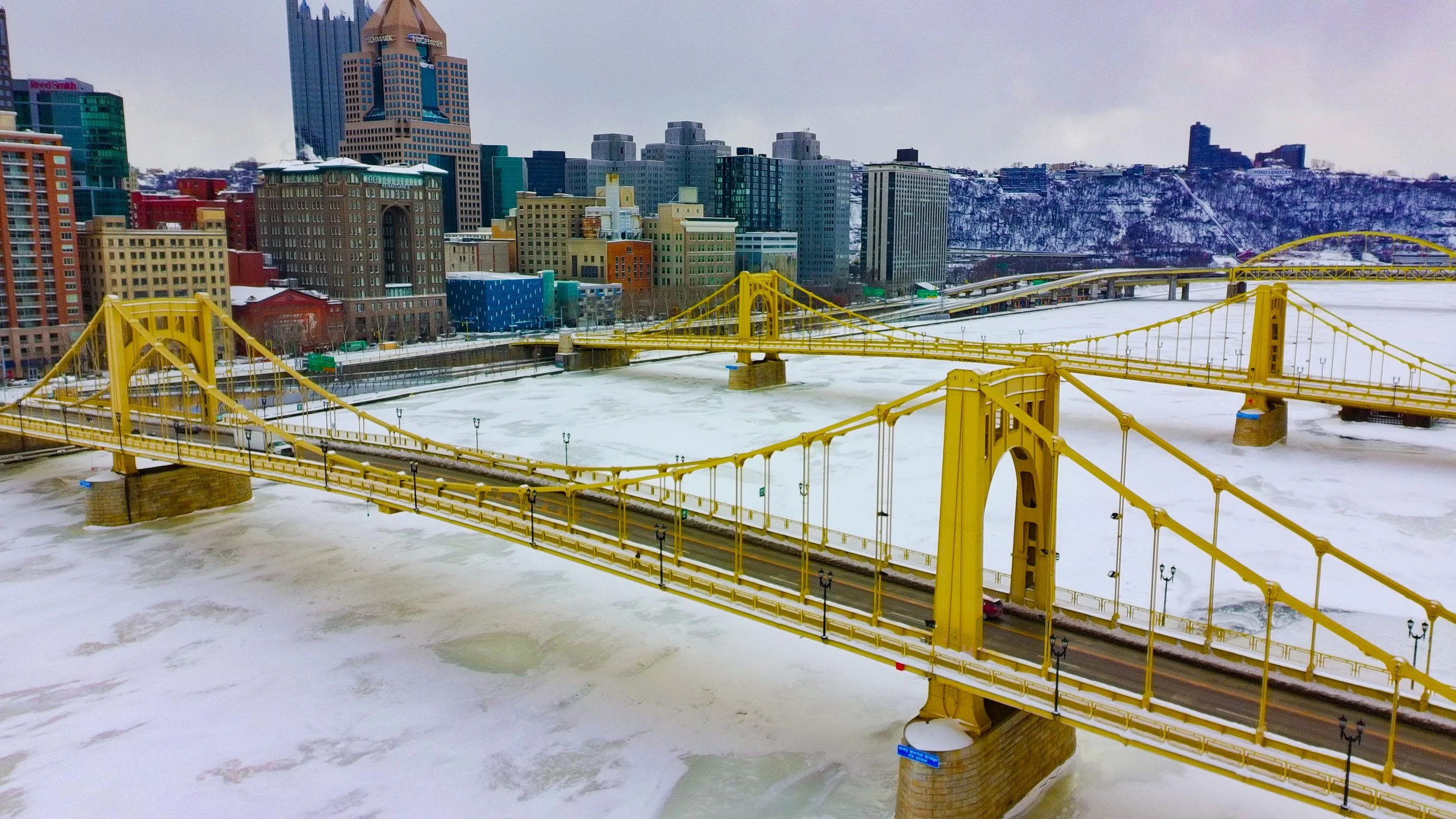 A drone flying in front of a suburban house with a lawn and trees.