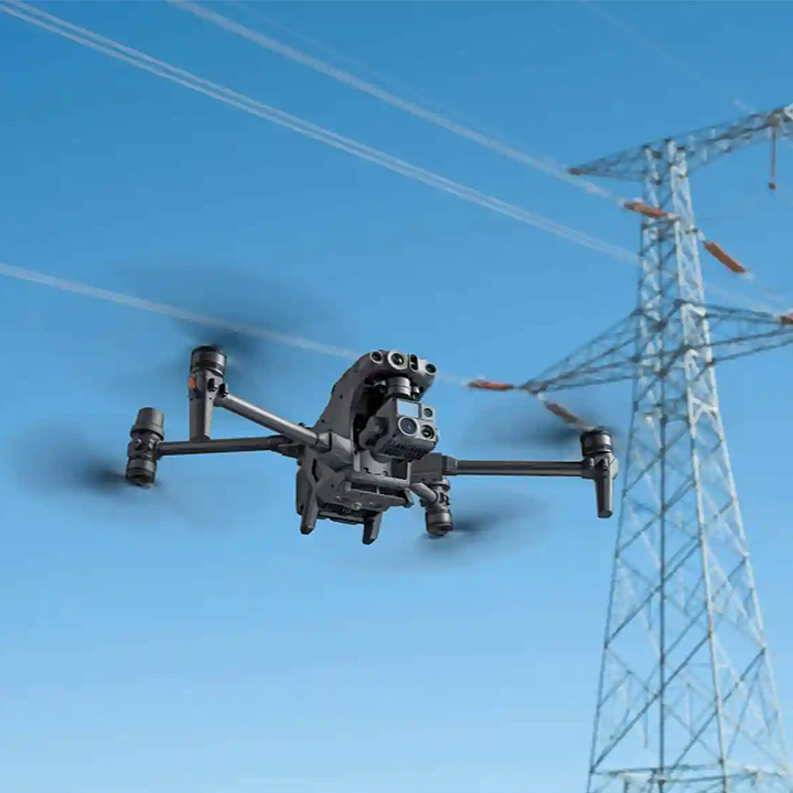 A drone flying near a power line tower against a blue sky.