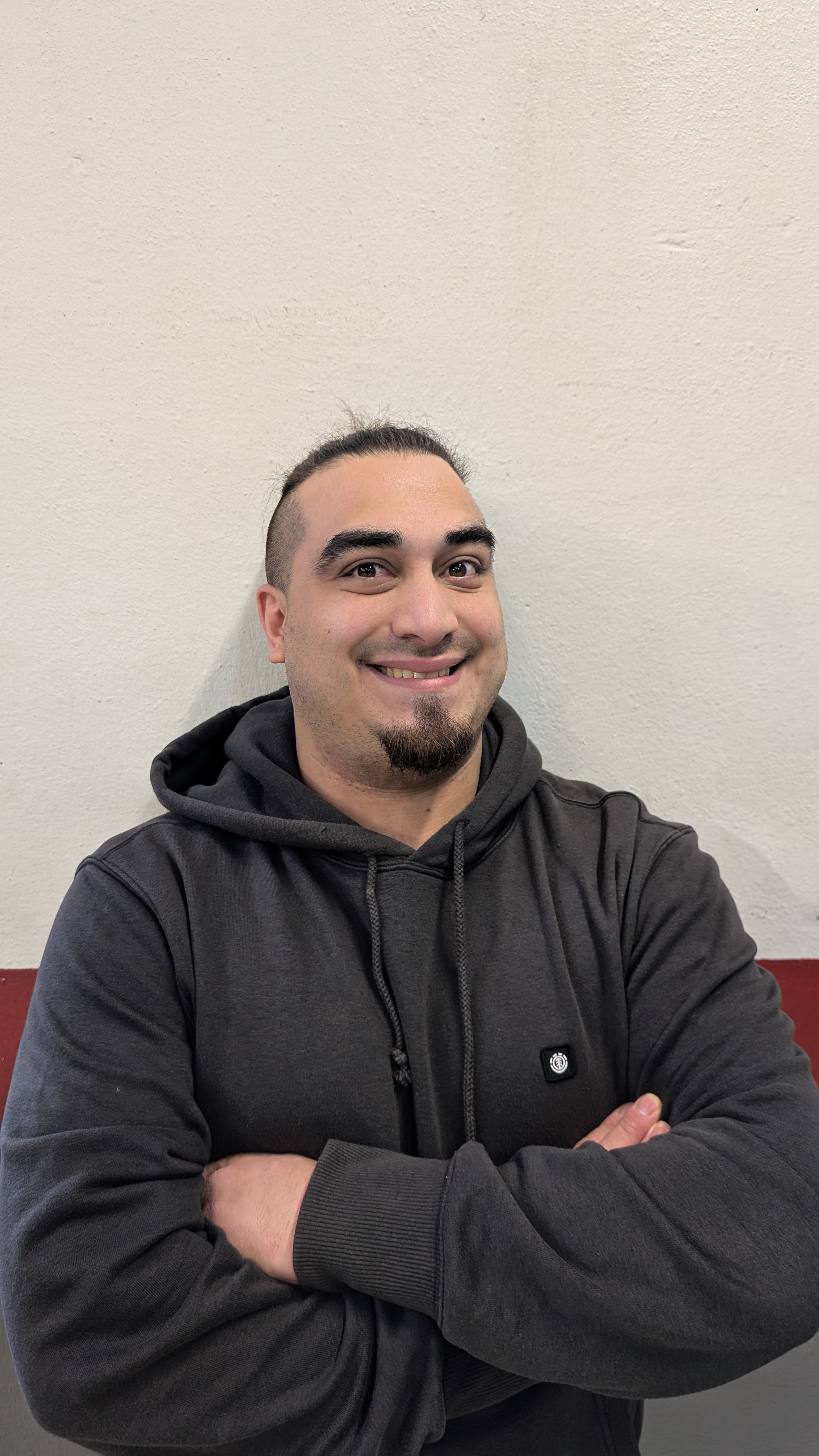 Ein junger Mann arbeitet unter einem Fahrzeug, leuchtet mit einer Taschenlampe und schaut nach vorne. Er befindet sich zwischen Autoreifen.