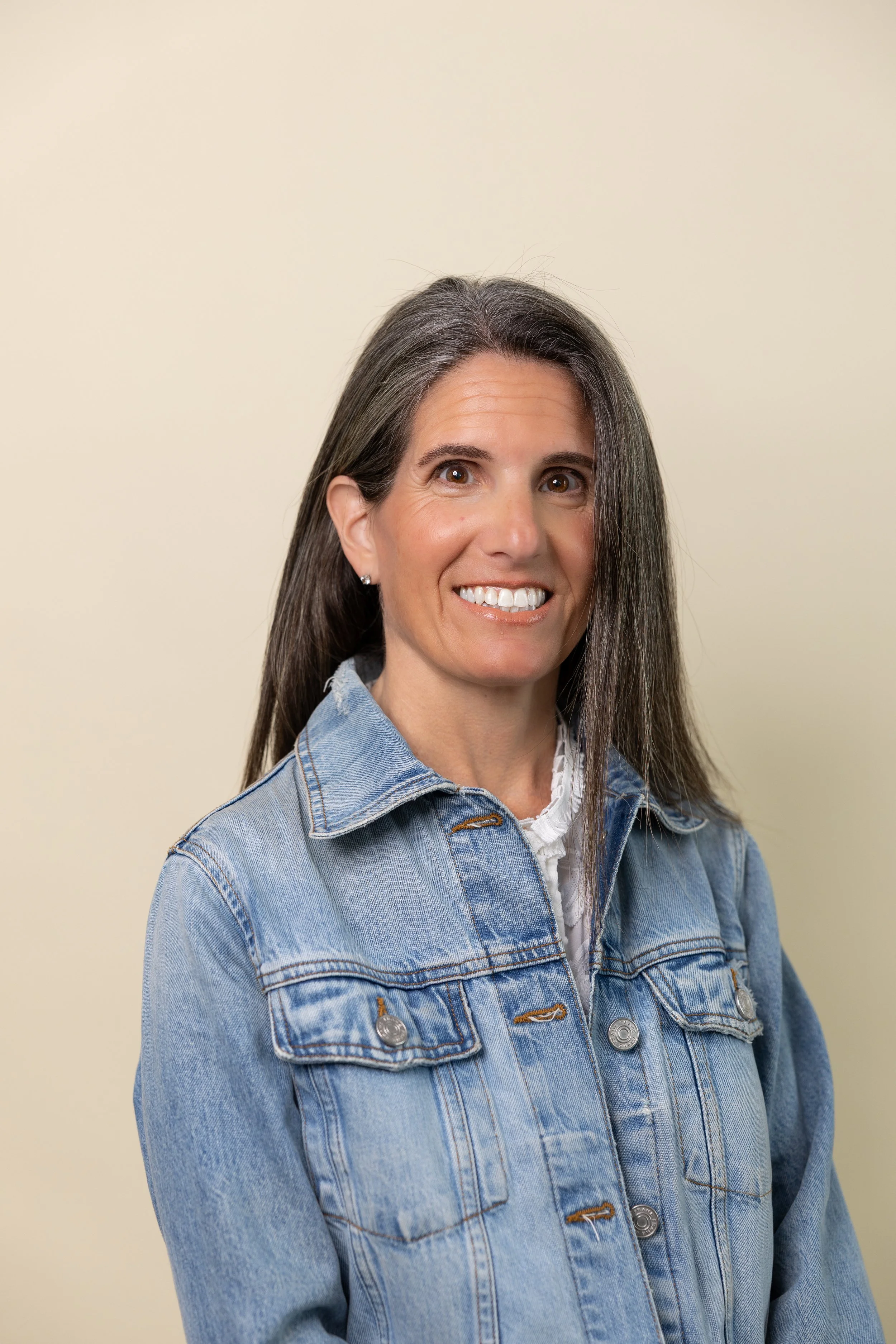 Portrait photograph of Tara Funk, the Founder of Roots and Wings Collective. Tara is smiling at the camera wearing a denim jacket.