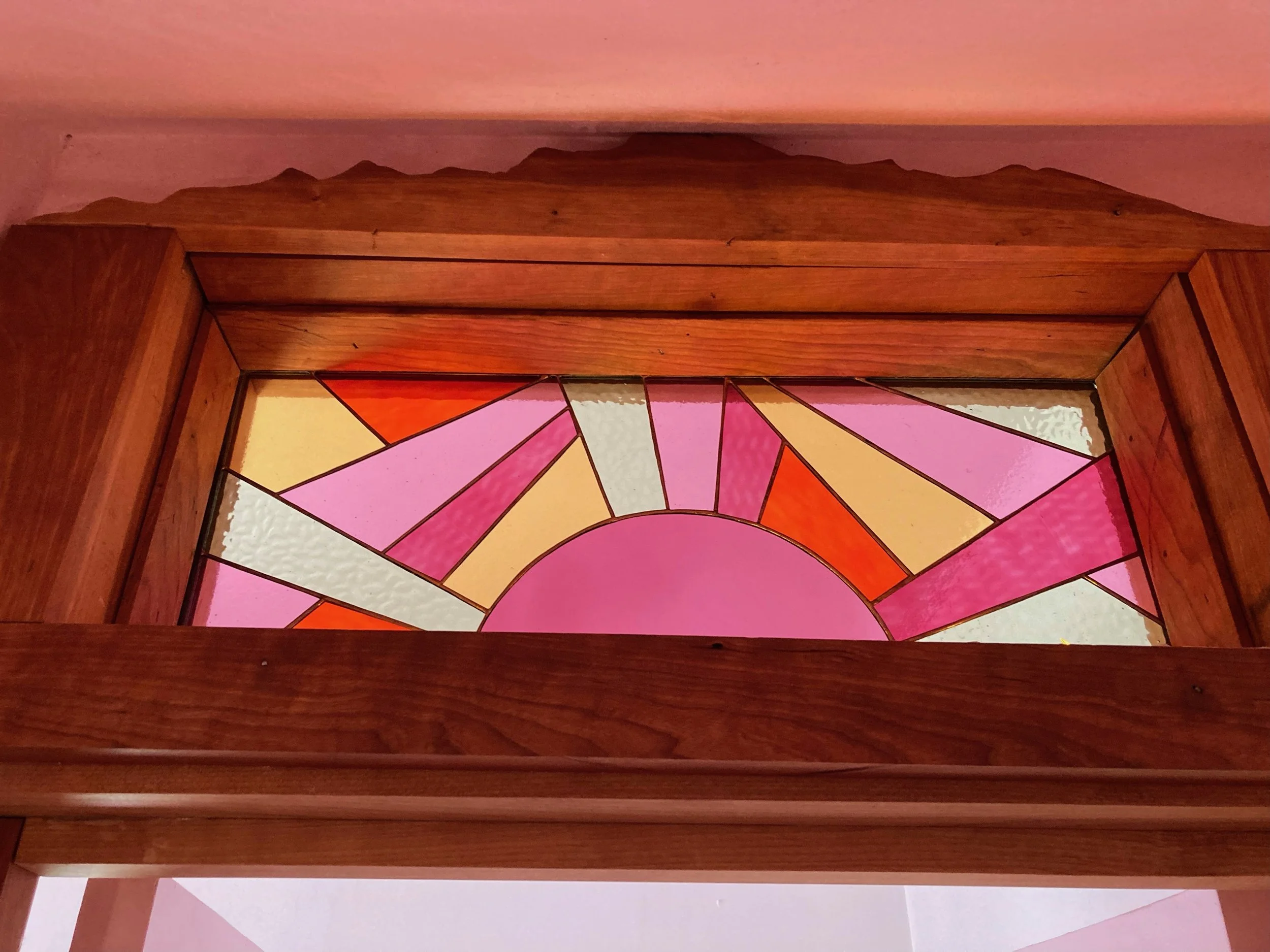 Decorative stained glass window with geometric shapes in pink, orange, yellow, and white, surrounded by a wooden frame.