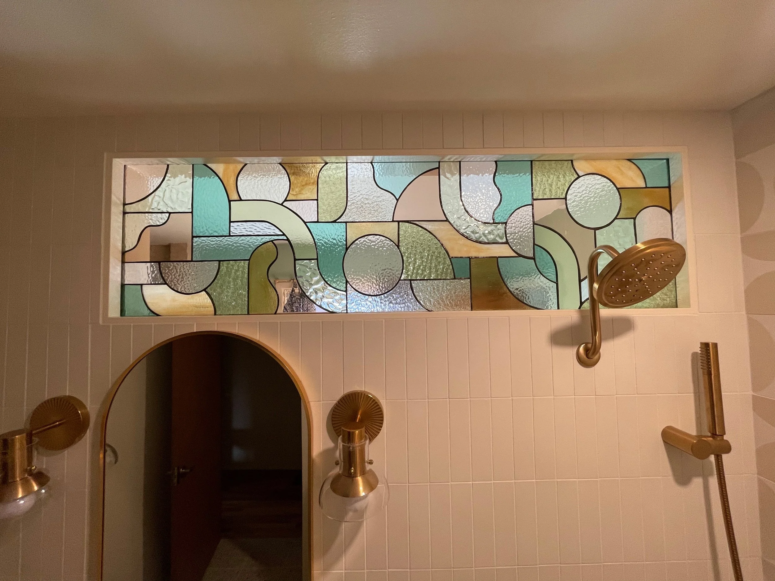 Bathroom with a stained glass window, gold showerhead, and a gold handheld shower wand.