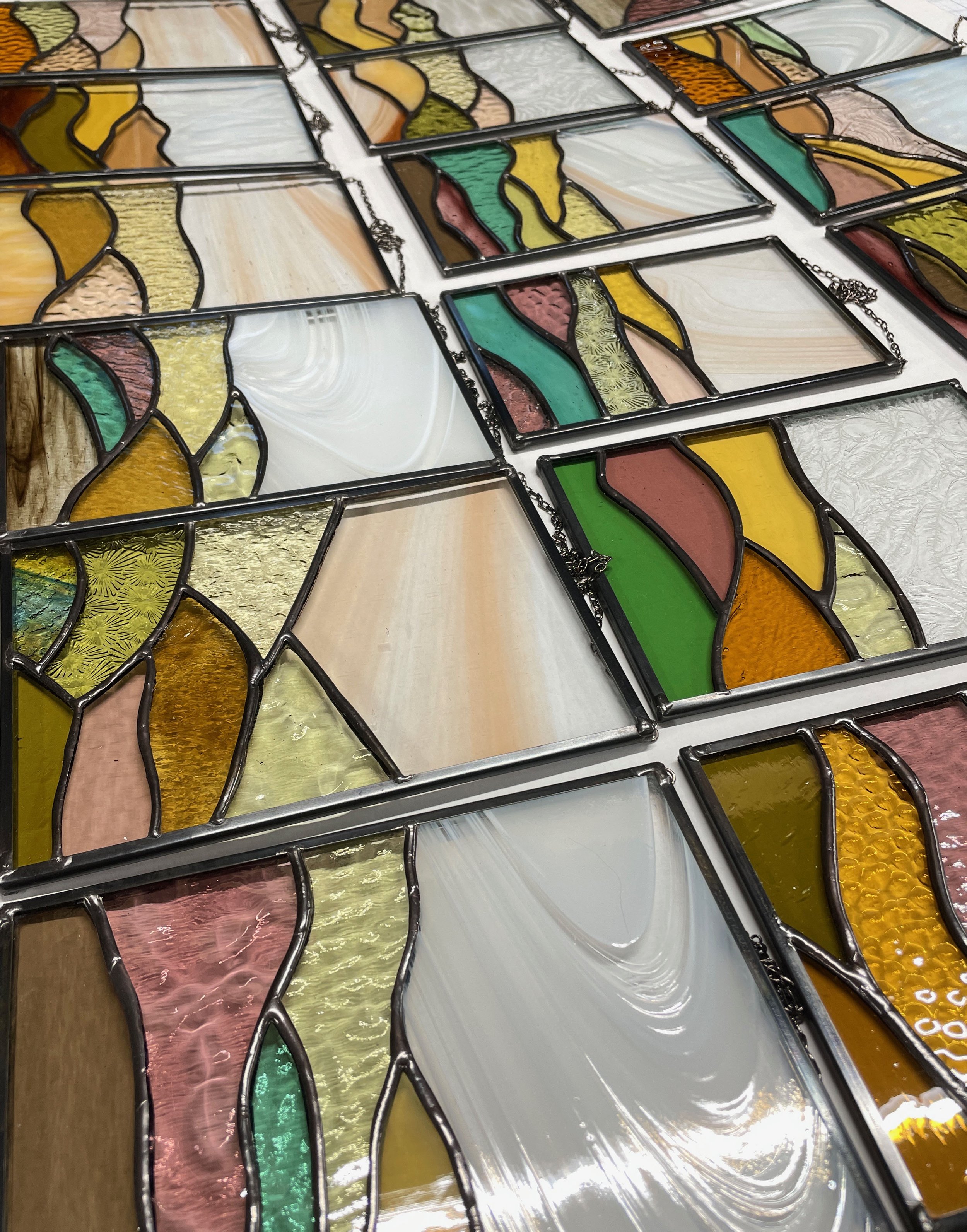Close-up of stained glass sun catchers showing an abstract landscape with yellow, pink, green, and clear glass.