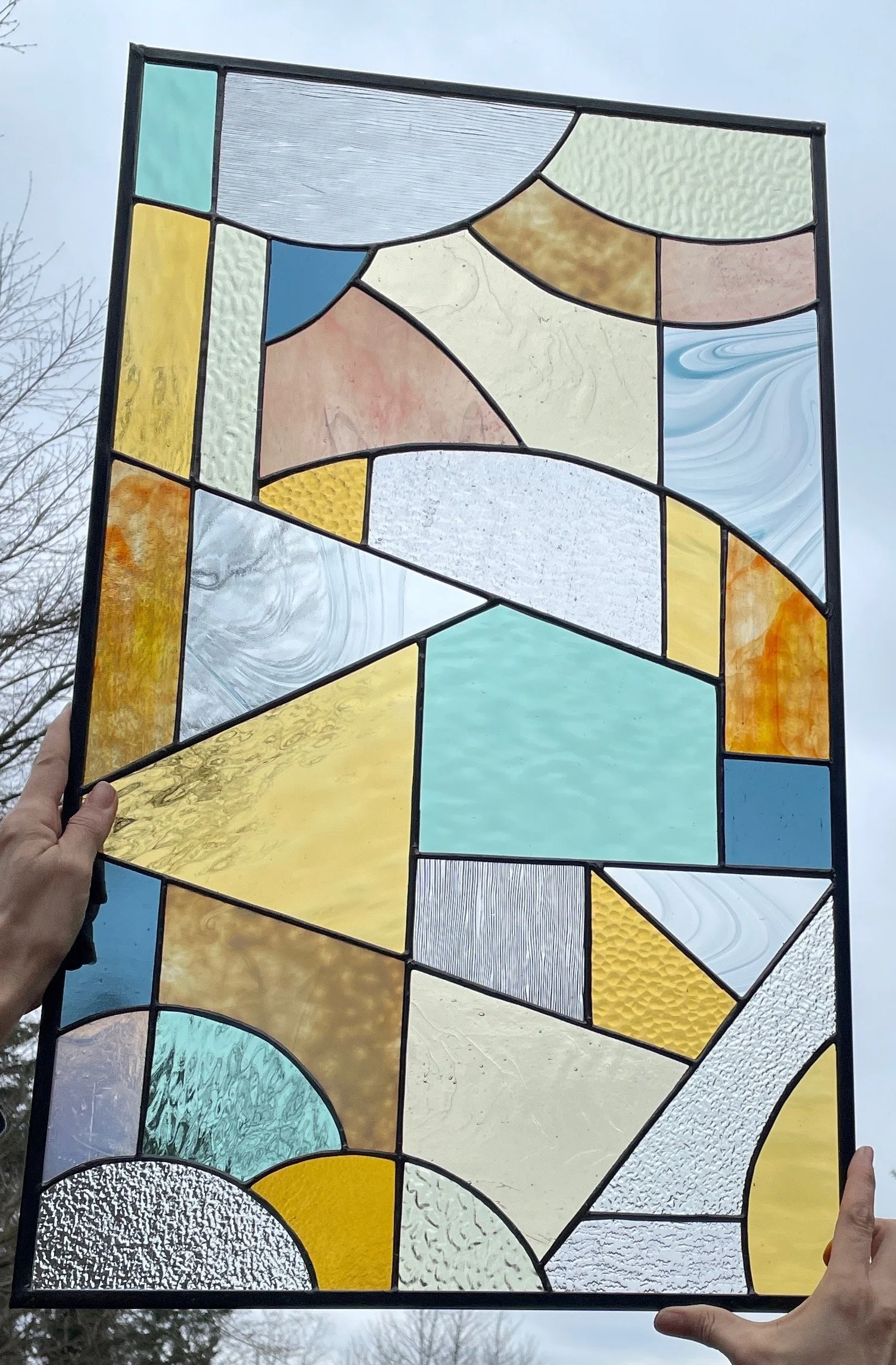 Colorful stained glass window with abstract geometric patterns, held up against an overcast sky.