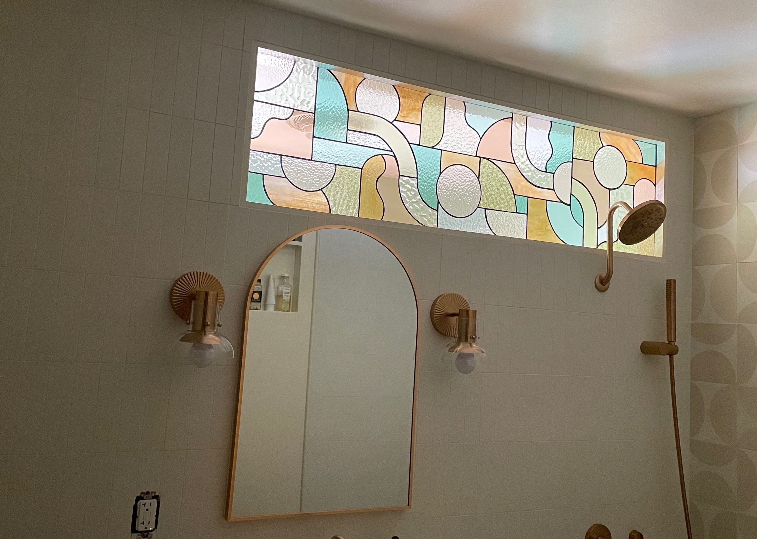 Bathroom with a stained glass window, mirror, wall-mounted lights, and a showerhead.
