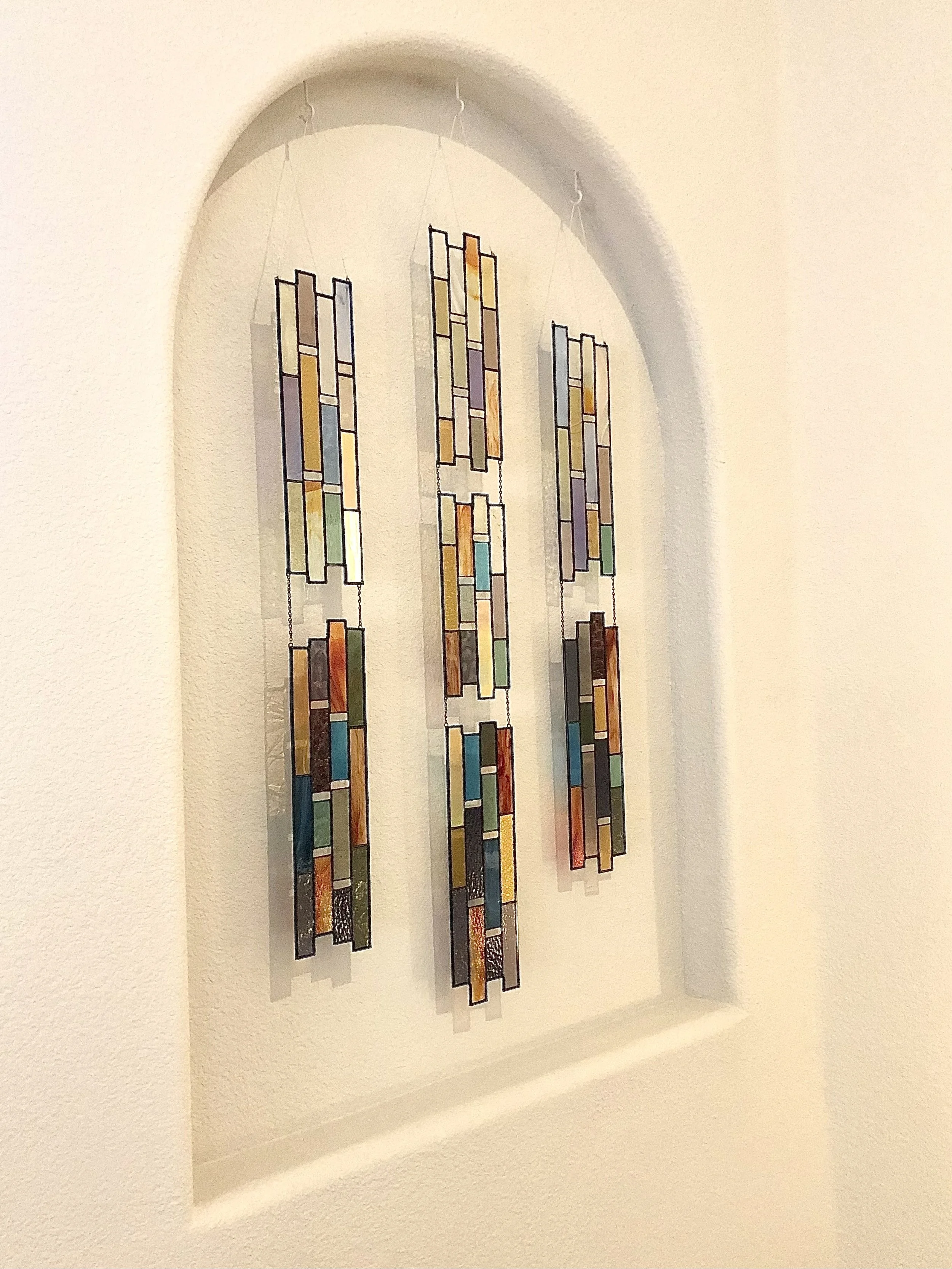 Colorful stained glass hanging art in an arched alcove on a beige wall.