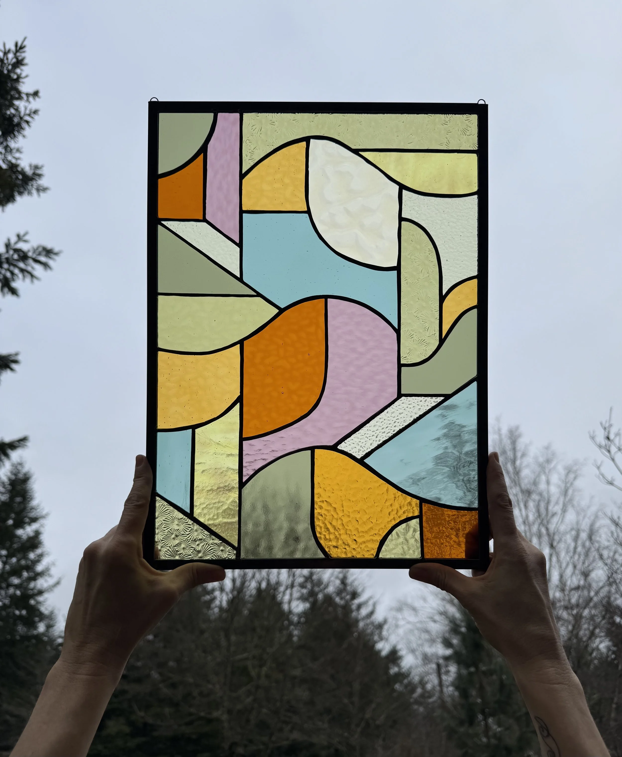 Person holding a stained glass artwork up against a cloudy sky, with trees in the background.