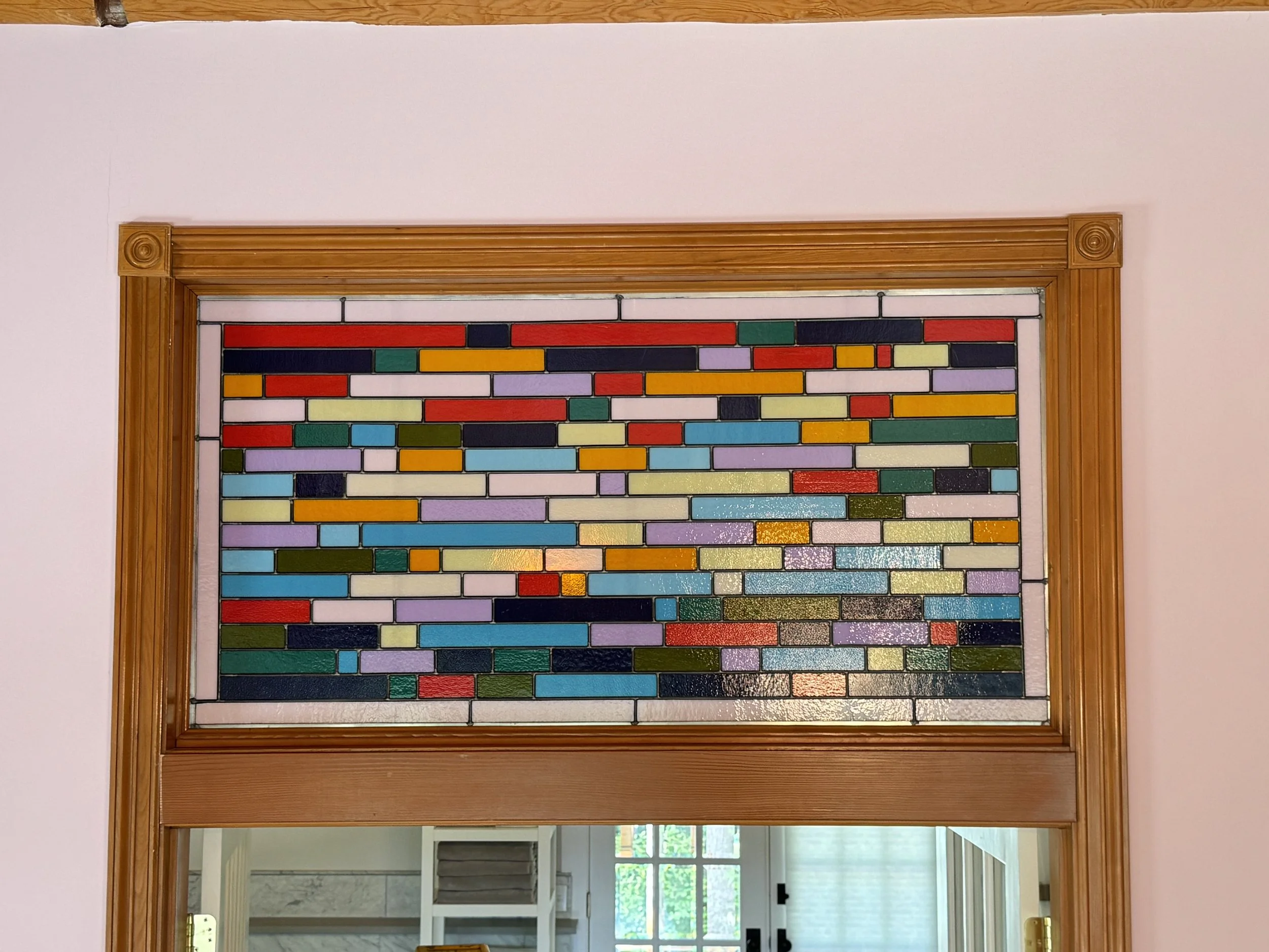 Colorful mosaic stained glass window above door frame with wood trim