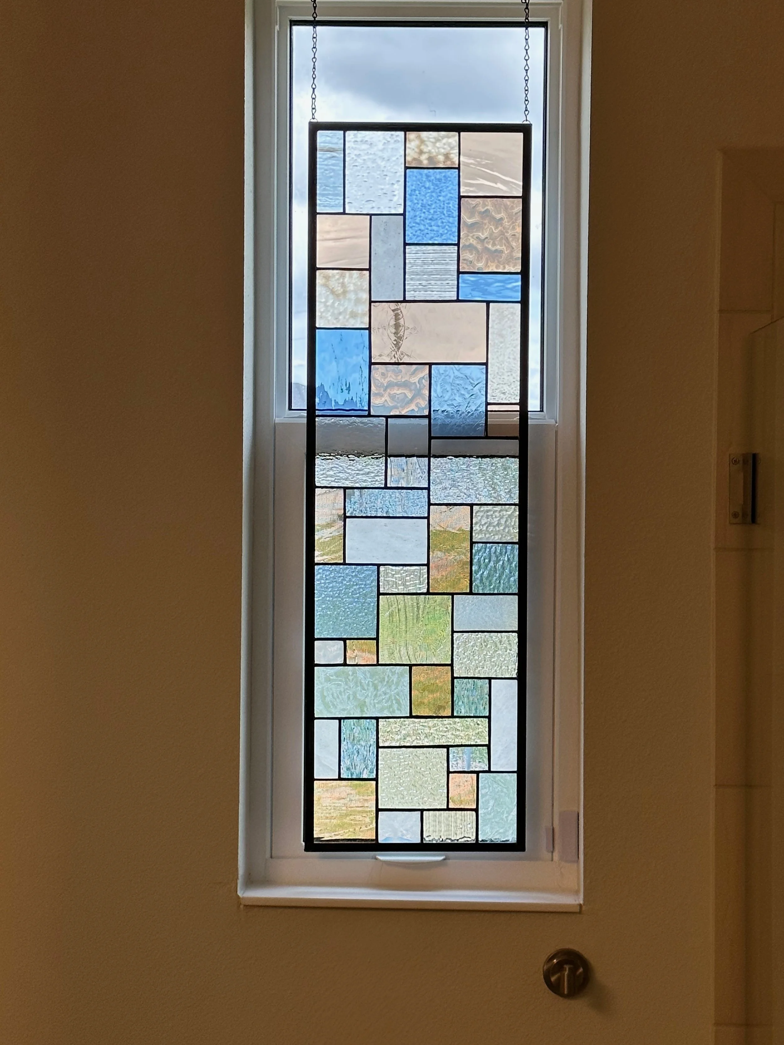 Decorative stained glass window with geometric patterns, hanging by chains inside a house, letting in natural light.