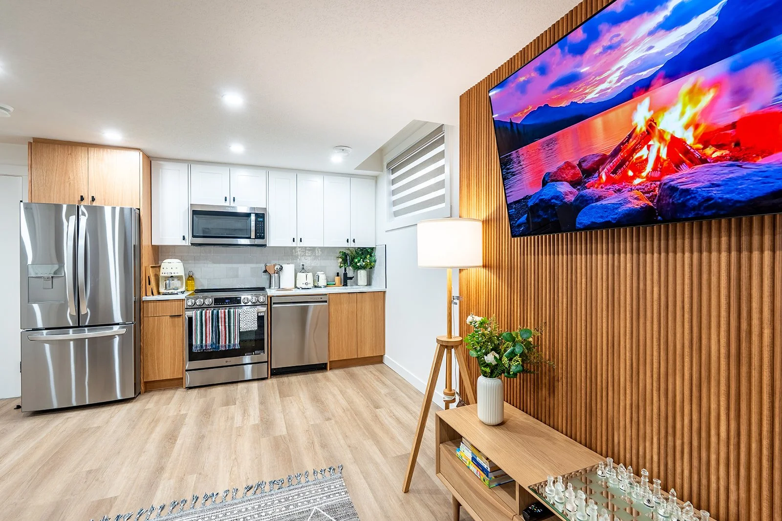 Modern Calgary legal basement suite with two-tone kitchen, stainless appliances, wood slat accent wall, TV, and light vinyl floors