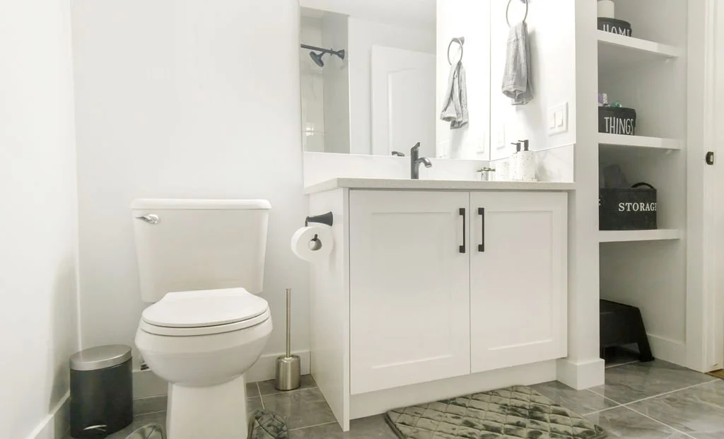 white bathroom with minimalist vanity, black hardware, grey marble tile floor, and green rug. Bright lighting accents clean contemporary decor.