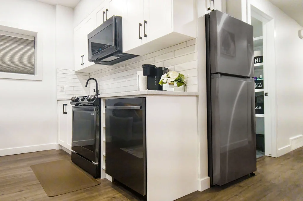 white shaker kitchen cabinets, black hardware, slate grey stainless steel appliances, white subway tile backsplash, dark wood plank flooring.