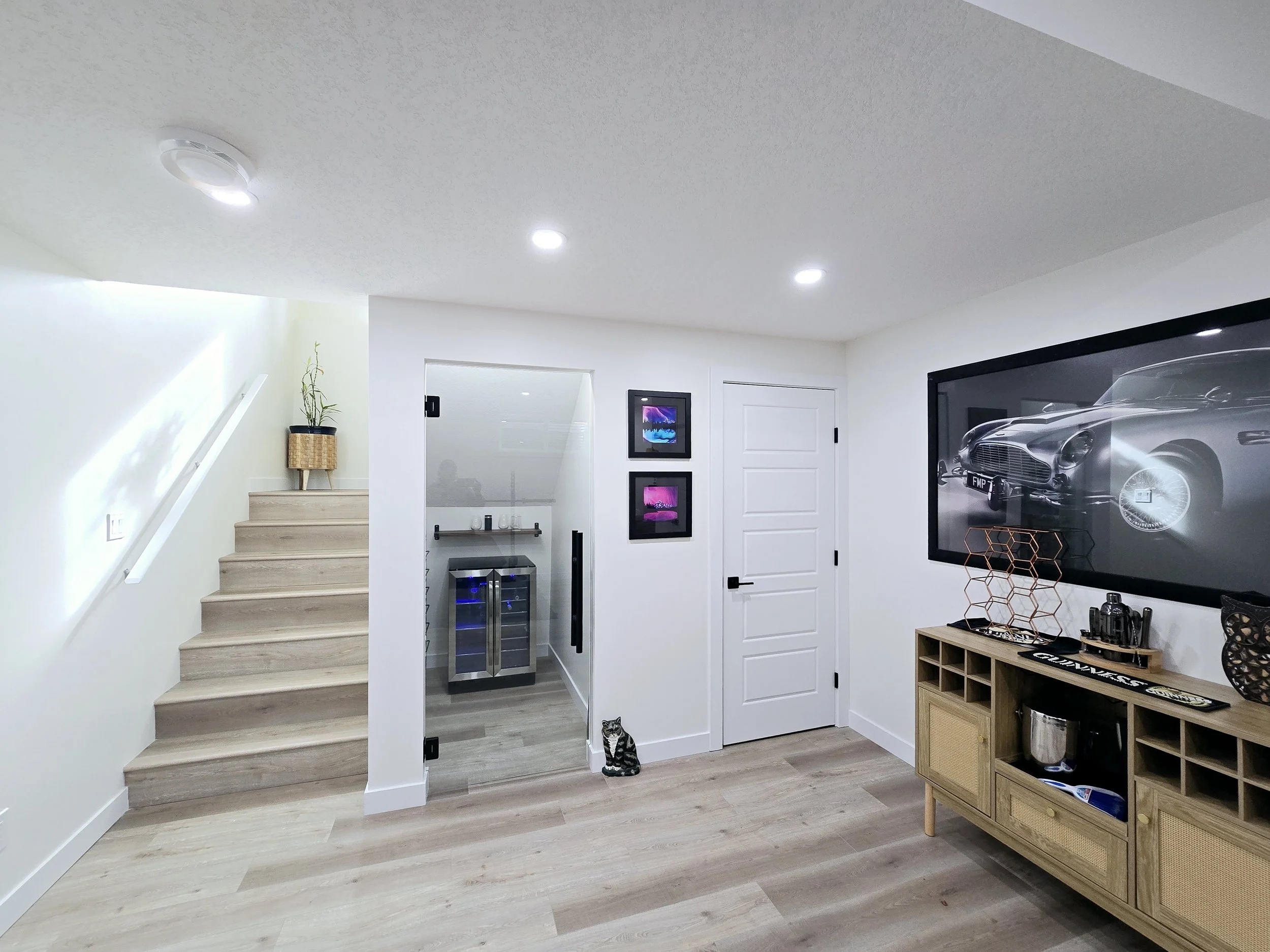 Modern Calgary basement renovation with light oak floors, glass wine cellar, blue-lit beverage cooler, bar sideboard, and recessed LEDs.