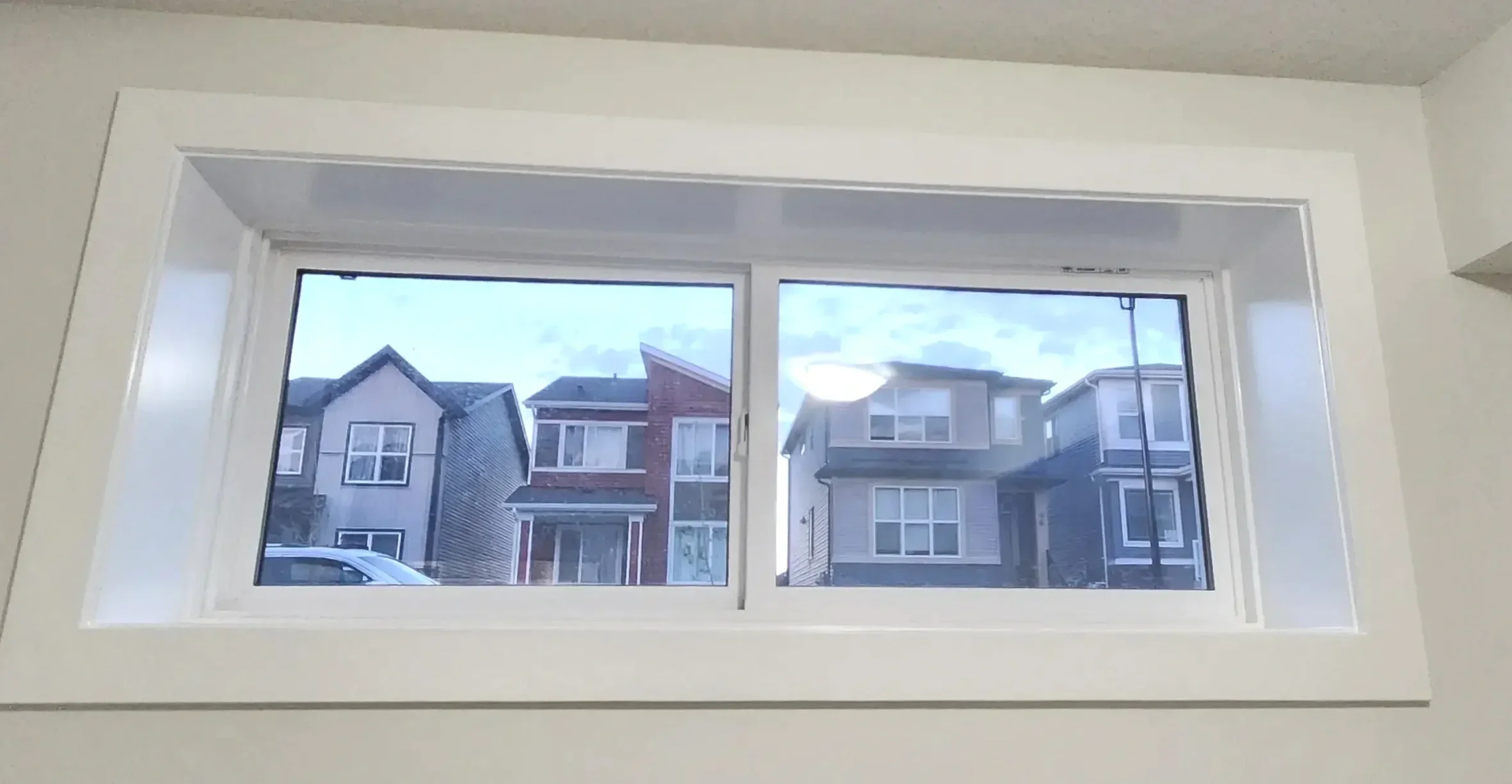 View of a neighborhood with modern houses seen through a double-pane window from inside a room with white walls.