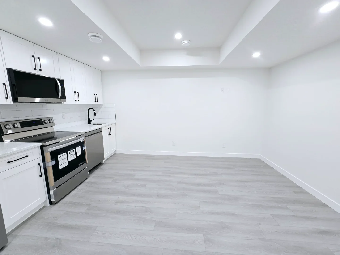 A wide-angle view of an empty open-concept living space with neutral white walls and light-toned wood-look flooring.
