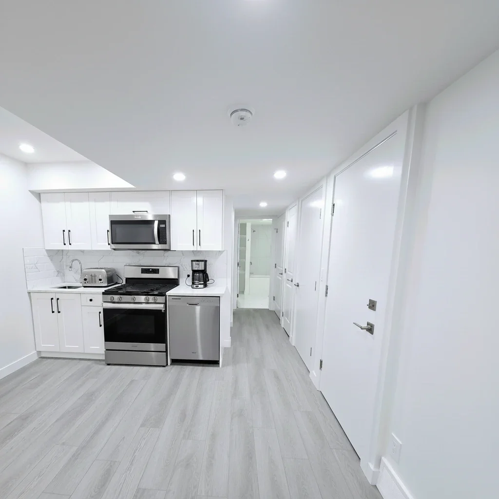 Modern white kitchen with stainless steel appliances and light grey wood floors in a minimalist bright apartment hallway. Keywords: modern kitchen, white cabinets, stainless steel appliances, grey wood flooring, apartment interior, minimalist design,