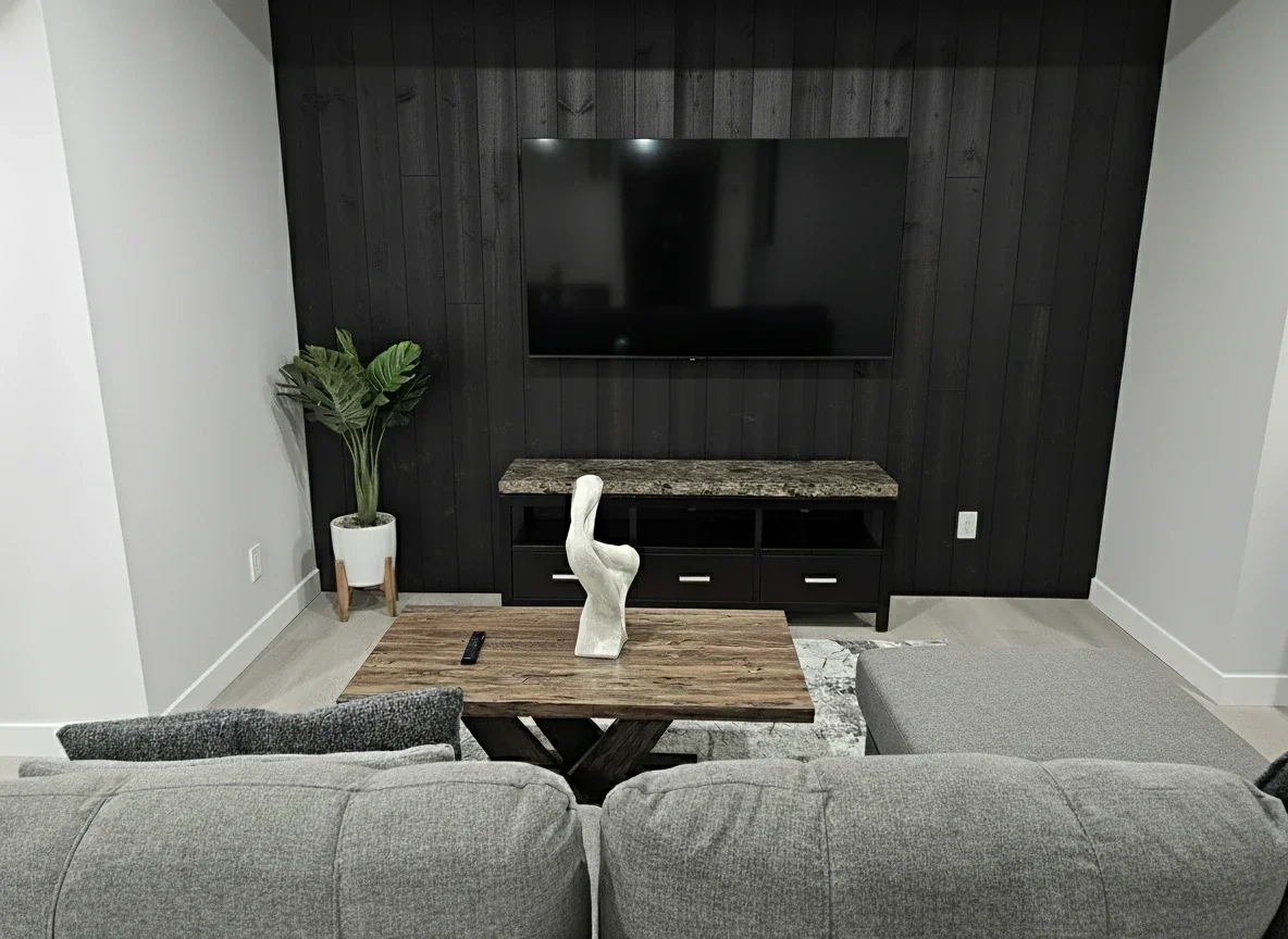  living room: black wood wall, mounted TV, grey sectional, rustic coffee table with white sculpture, stone-top console, and potted green plant.