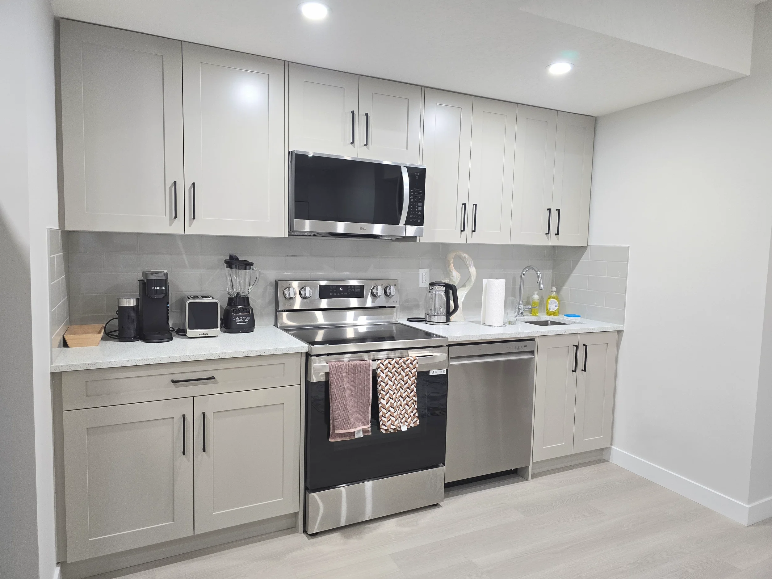Modern kitchen with light grey shaker cabinets, white quartz countertops, grey subway tile backsplash, and stainless steel LG appliances.