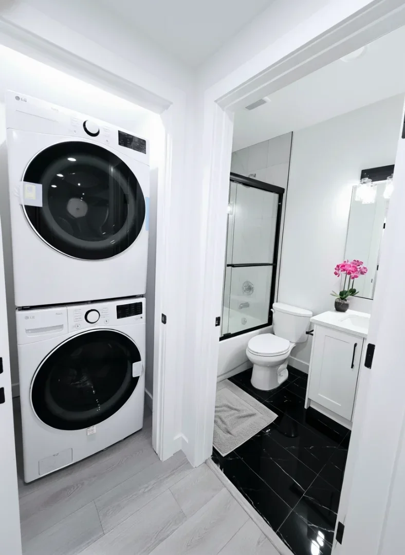 A functional space featuring a stacked LG washer and dryer next to a bathroom with black marble-style tile.