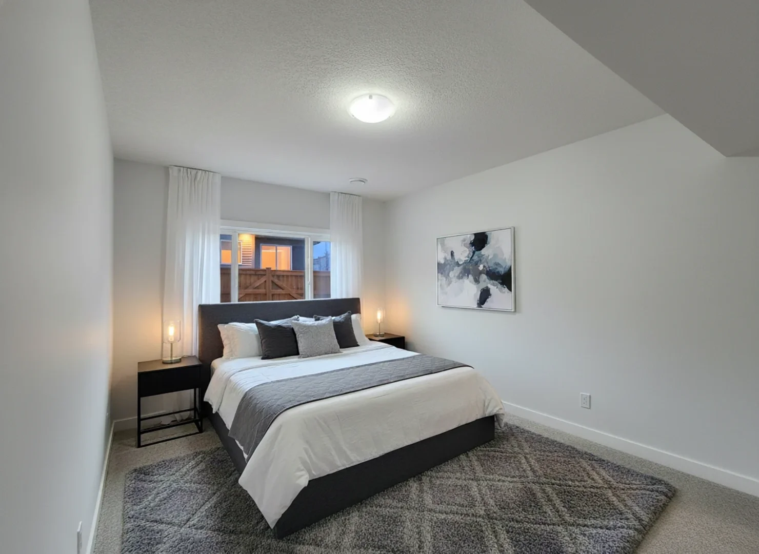A sophisticated bedroom with a dark grey upholstered headboard, white and grey bedding, and modern glass-encased bedside lamps.