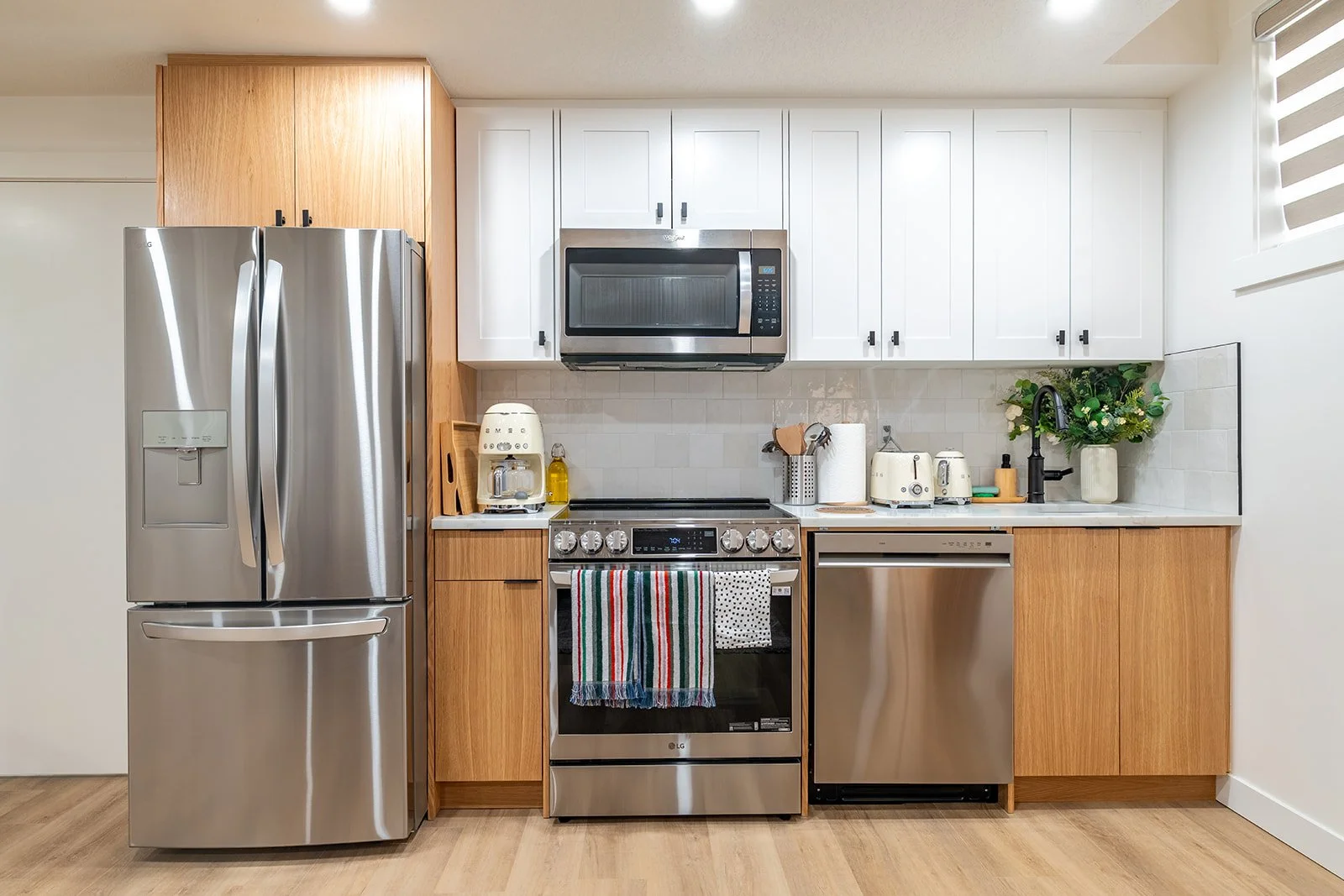 Modern open-concept living room and kitchen with white cabinetry, black hardware, a coffee maker, a gray sofa, a round coffee table, artwork, and a rug.