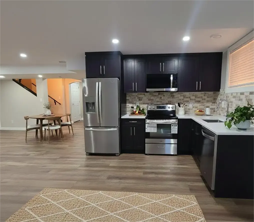 Modern dark navy kitchen, stainless steel appliances, white quartz counters, stone backsplash, wood floors, jute rug, bright recessed LED lighting.