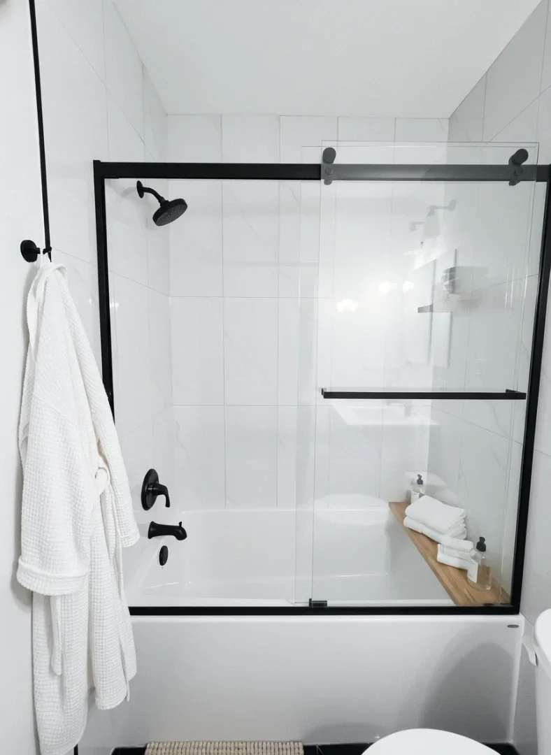 A contemporary bathroom showing a white bathtub with trendy matte black fixtures and a sliding glass door.