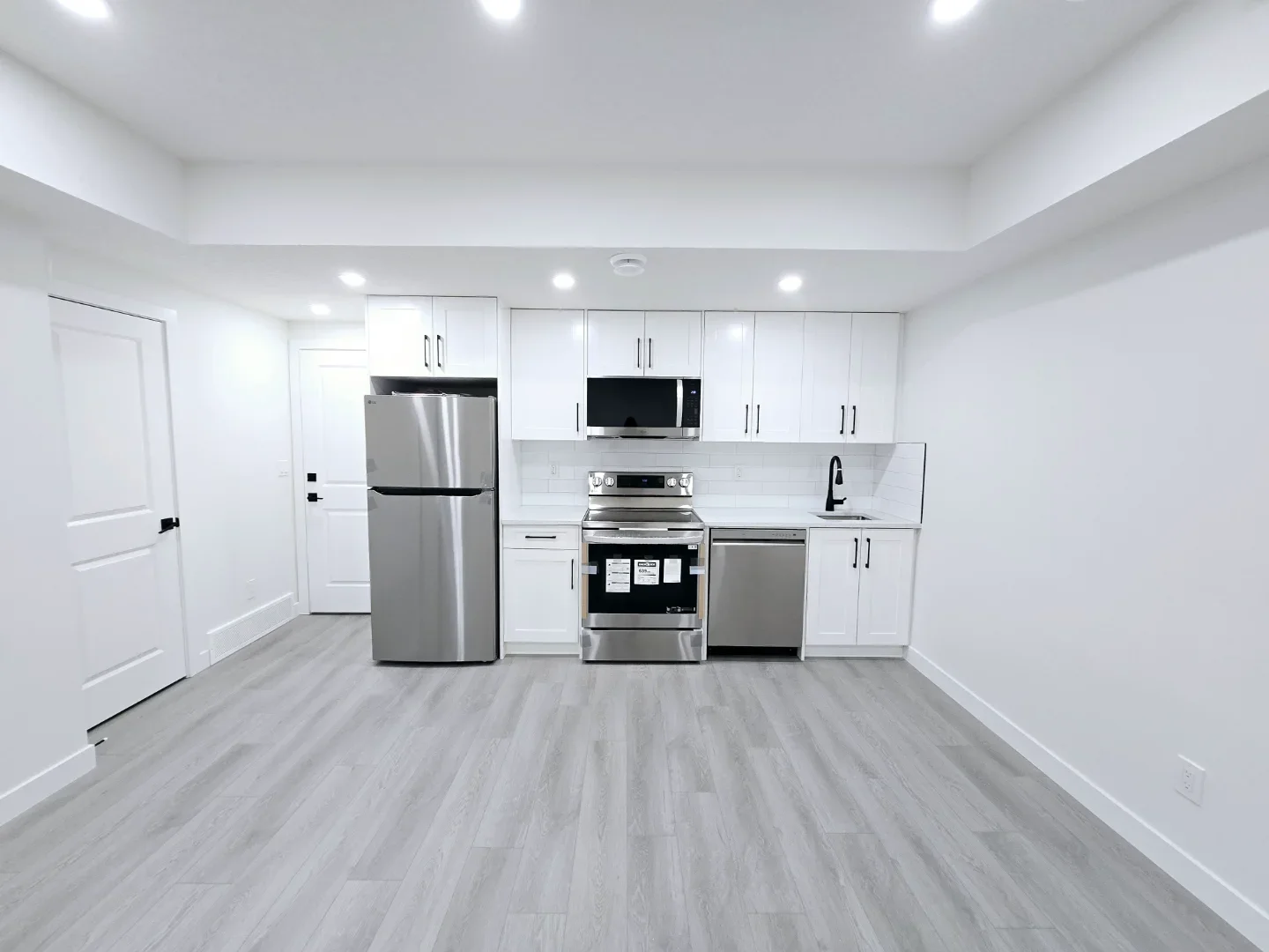 A bright, modern kitchen featuring white shaker cabinets, black hardware, stainless steel appliances, and luxury vinyl plank flooring.