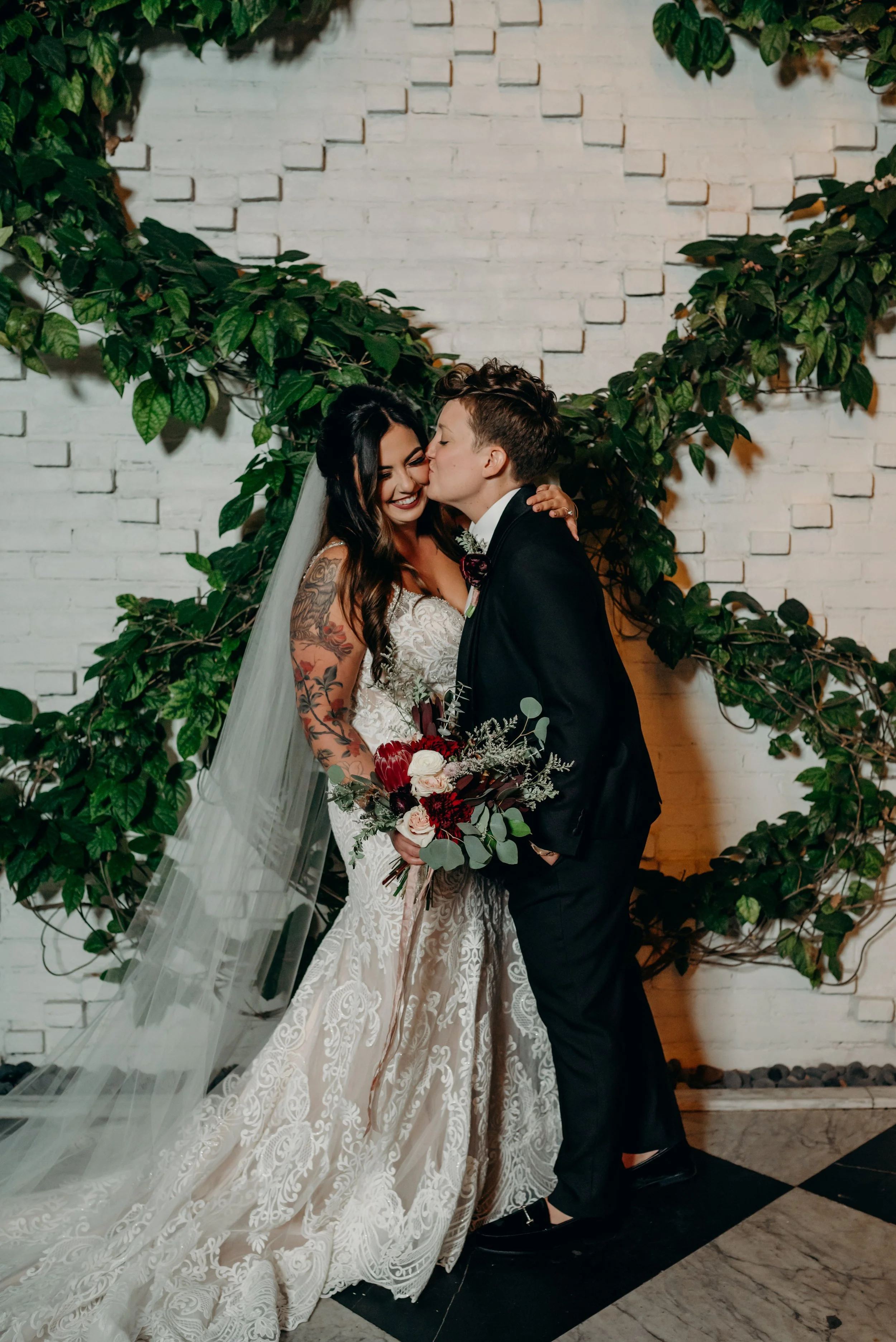 lgbtq+ wedding couple at oxford exchange tampa in front of white brick wall with greenery