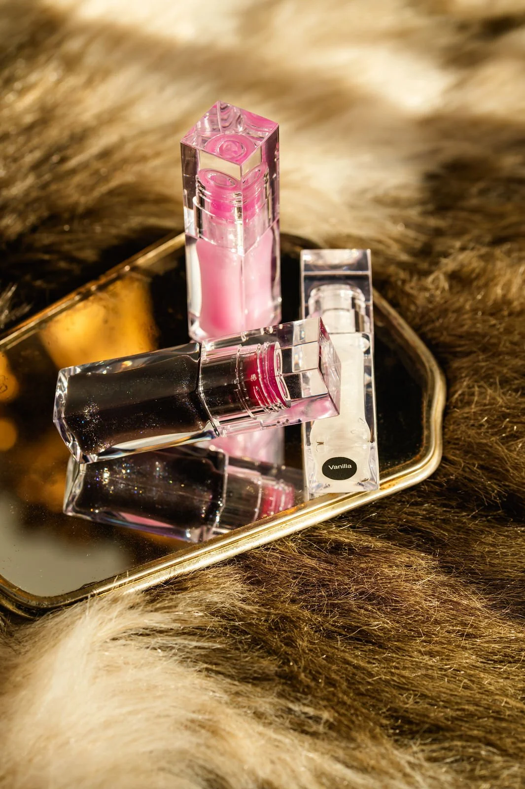 Three bottles of perfume or cosmetic products on a reflective gold-colored tray surrounded by brown and gray animal fur.