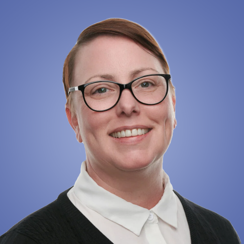 A woman with short brown hair, glasses, and light makeup, smiling against a blue gradient background, wearing a white collared shirt and a black sweater.