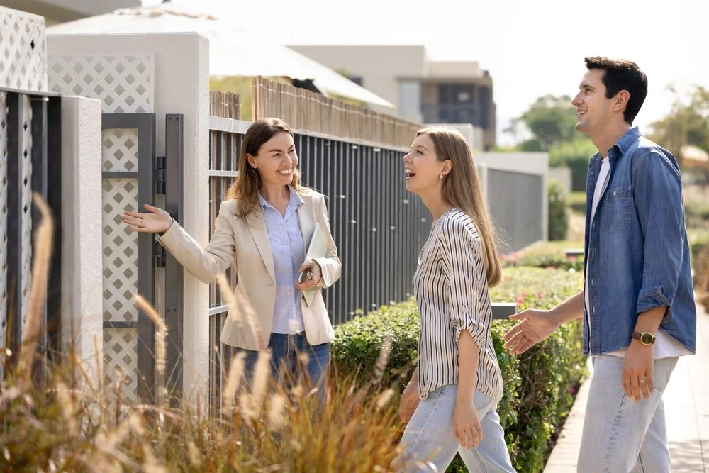 A real estate agent showing a house to a young couple outside on a sunny day.