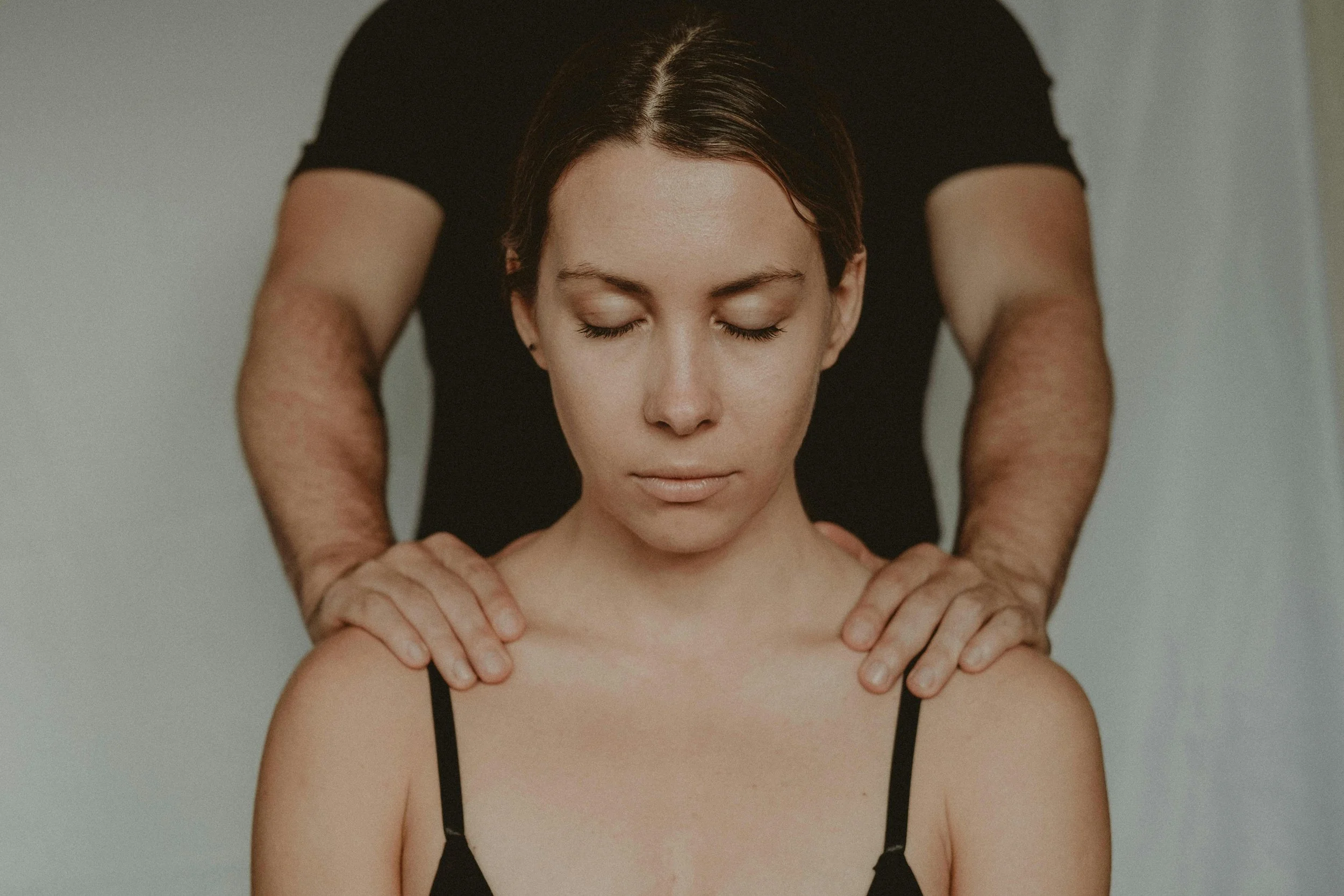 A woman receiving a massage, with a massage therapist applying pressure to her shoulders. The woman has closed eyes and appears relaxed.