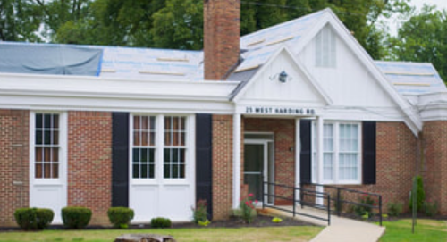 Front view of a brick building with white siding, multiple windows, a sign reading '20th District Hearing Office,' and a ramp leading to the entrance.