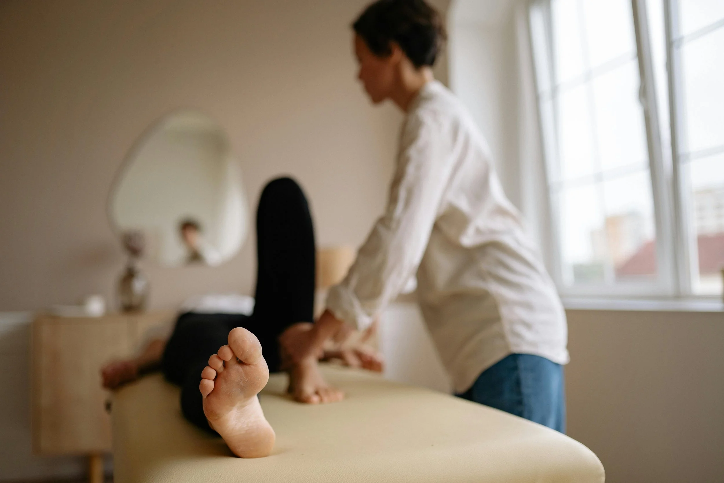Person receiving a massage on a massage table, with their foot in the foreground and a window in the background.