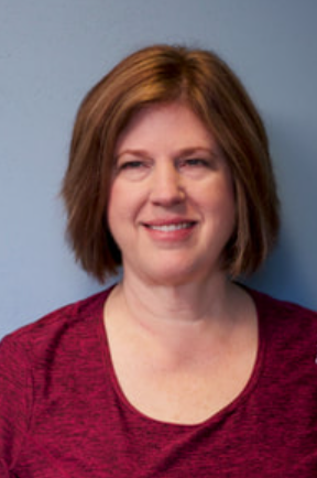 Woman with short brown hair wearing a red top smiling in front of a plain background.
