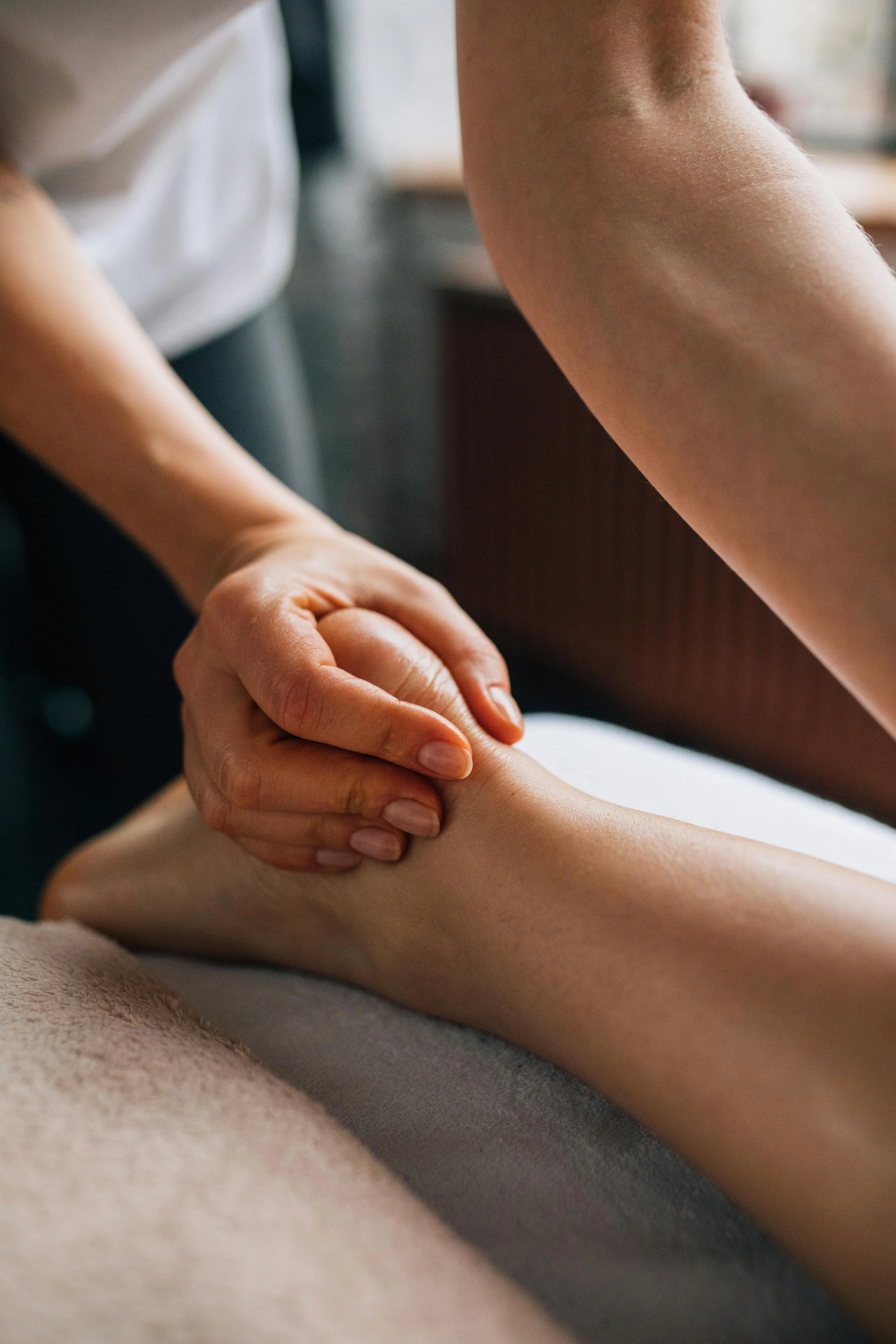 A massage therapist applying pressure to a person's calf muscle with their hands in a spa or massage setting.
