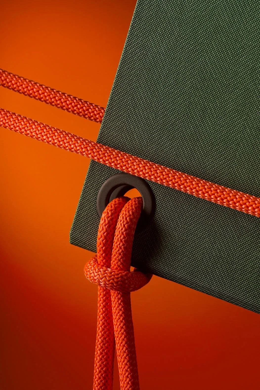 Close-up of a green textured object with an orange rope passing through a hole, tied in a knot, against an orange gradient background.
