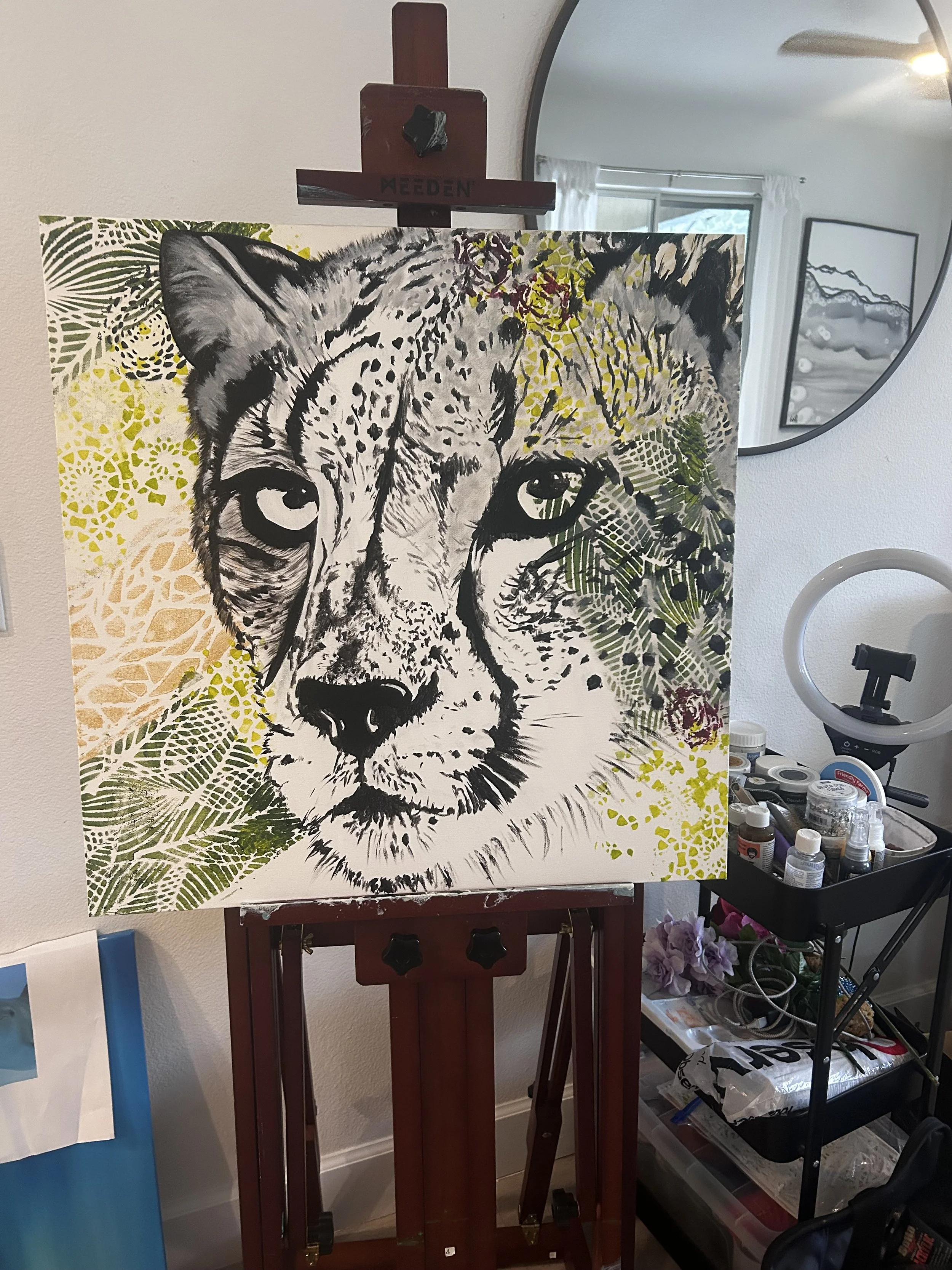 A canvas painting of a cheetah's face with detailed black and white fur, surrounded by colorful, intricate patterns and leaf designs.