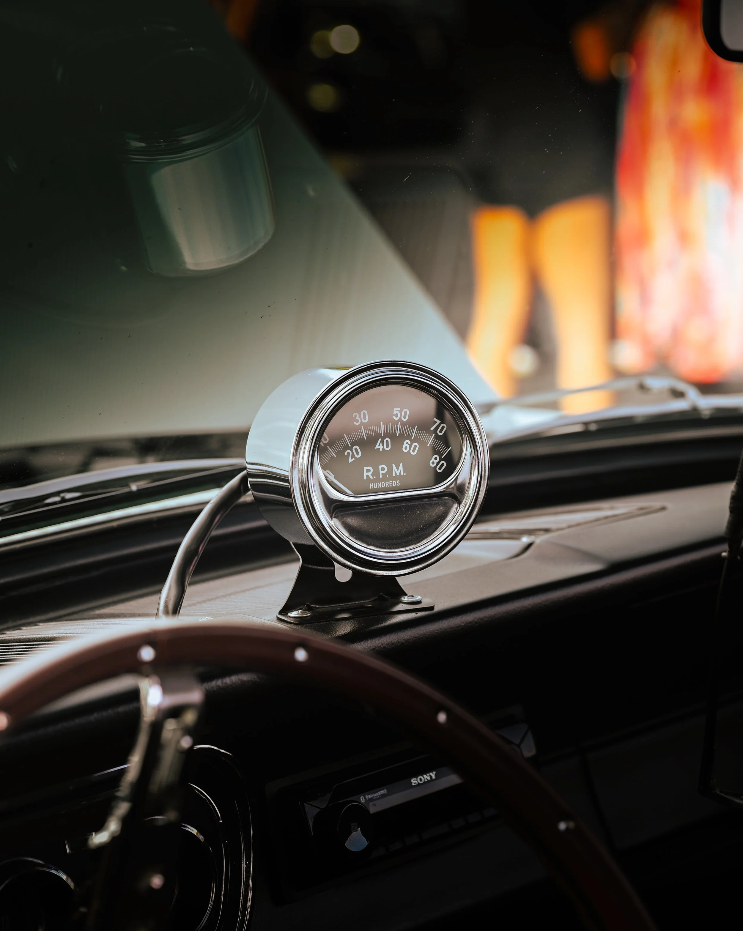 Close-up image of a car dashboard featuring an RPM gauge, steering wheel, and a digital display, with some background elements blurred.