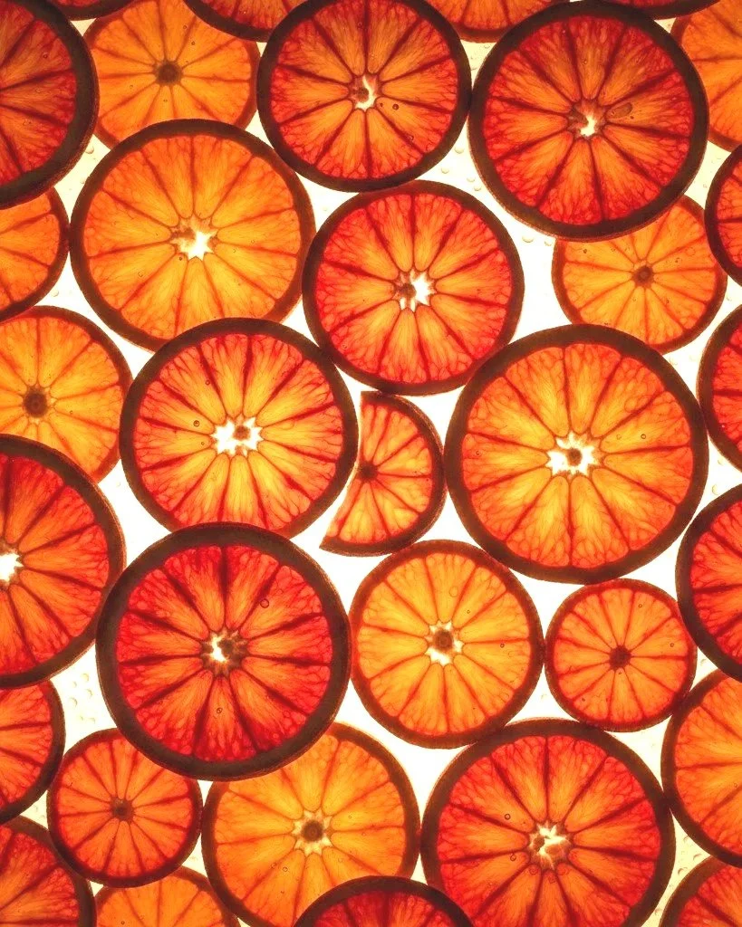 Close-up view of orange and red citrus slices, possibly blood oranges, arranged on a backlit surface to highlight their bright colors and internal patterns.
