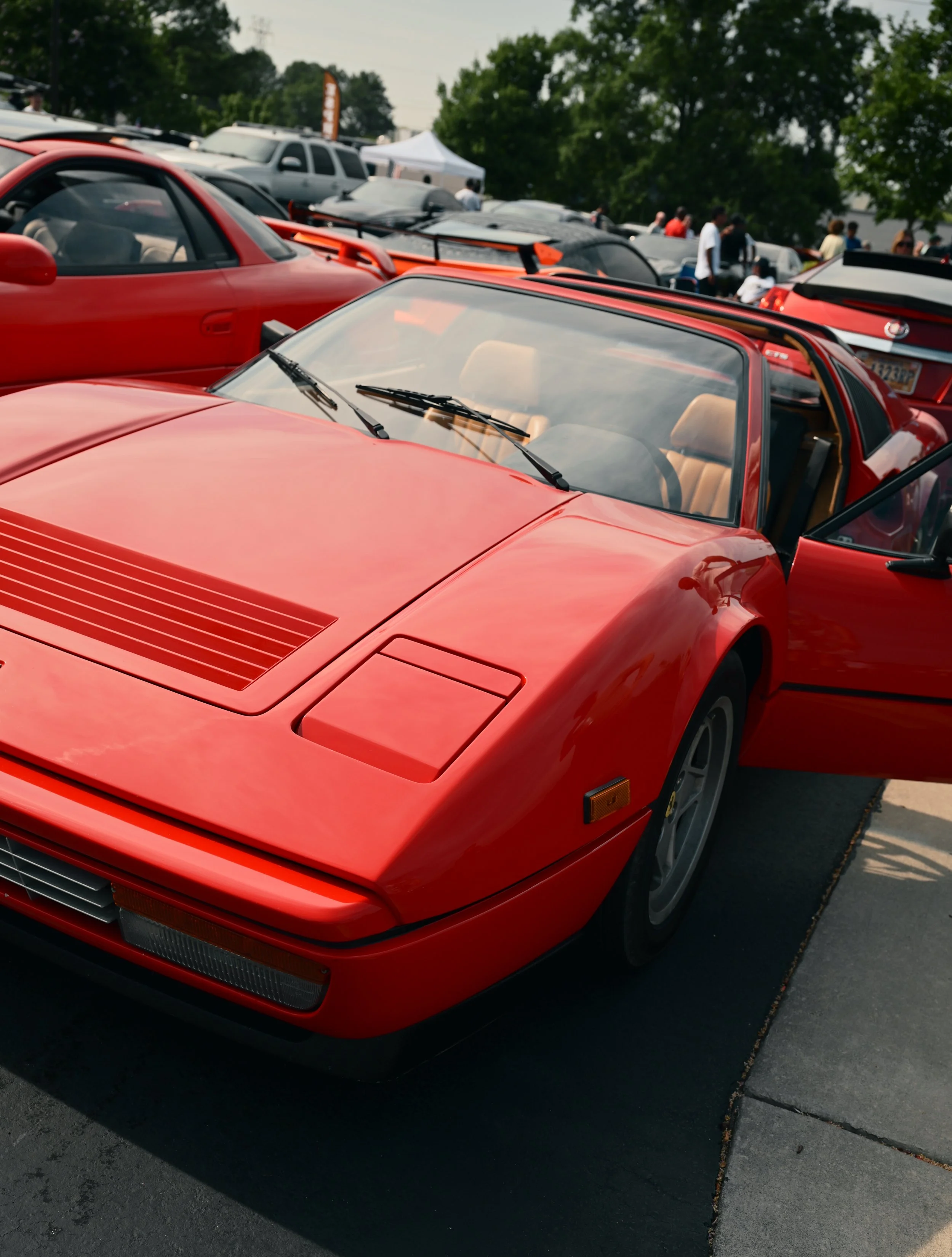 A red vintage Ferrari sports car parked at a car show with other cars and people in the background.